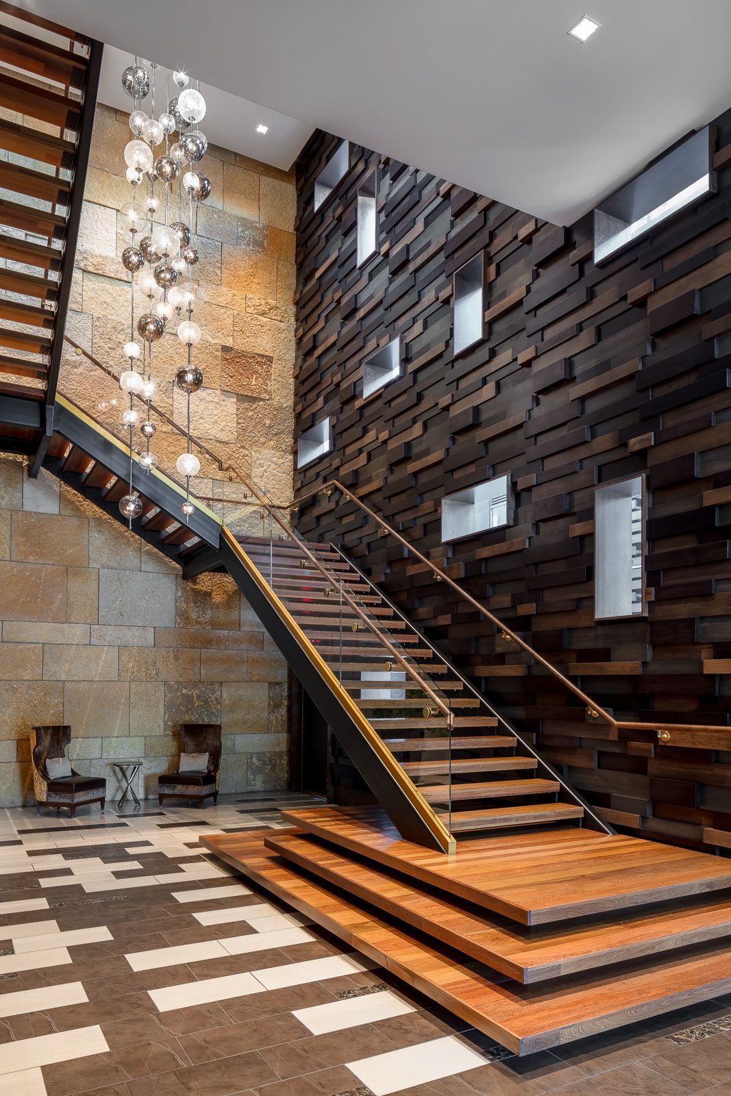 Two-story lobby with a wooden staircase, glass railings, and a hanging globe chandelier.