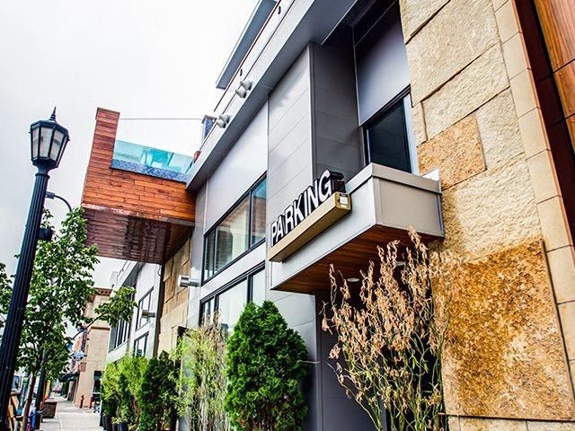 Exterior view of a modern apartment building with a parking sign and greenery.