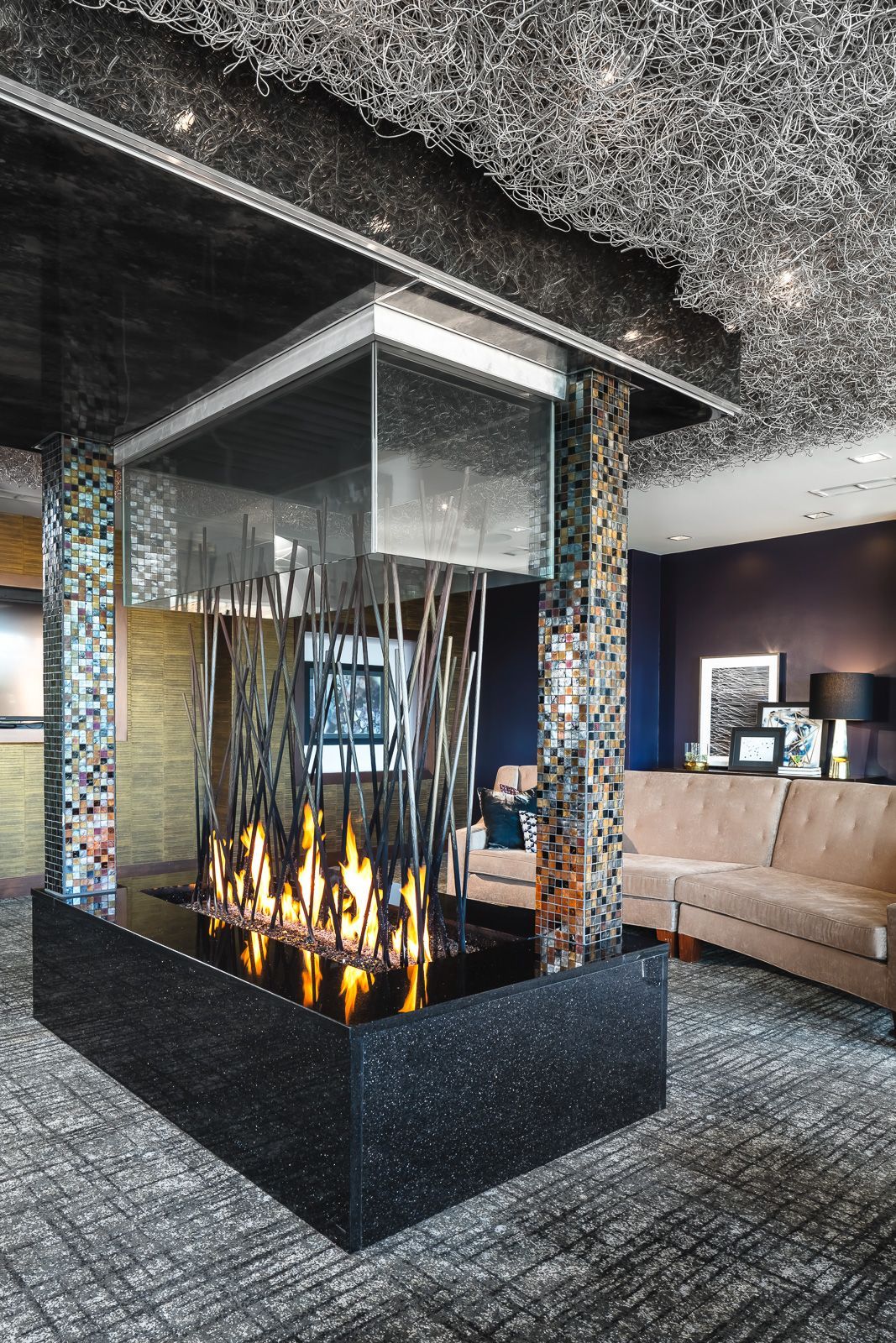 Interior community lobby with a glass-enclosed fireplace and mosaic-tile columns