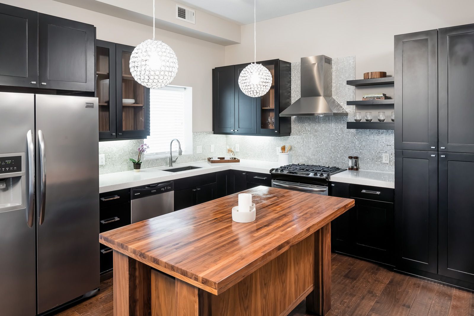 Modern kitchen with black cabinets, stainless steel appliances, and a large wooden island.