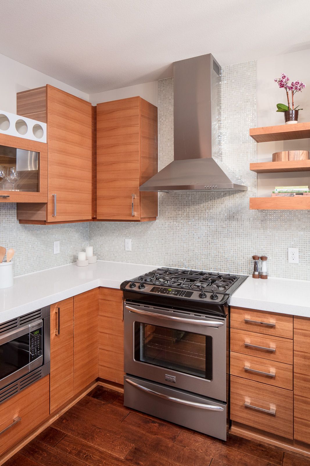 Modern apartment kitchen with stainless steel stove, vent hood, and wood cabinets.