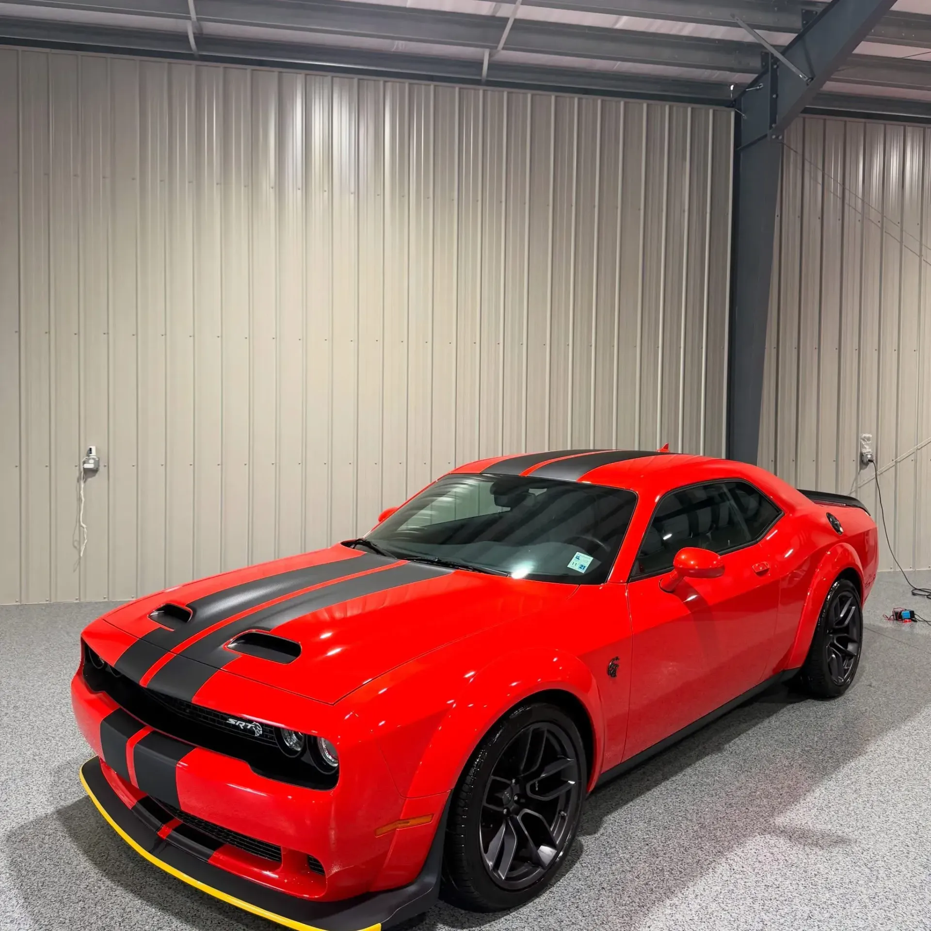 Red Dodge Challenger with black racing stripes parked in a garage.