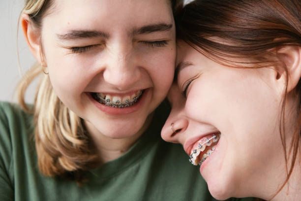 Two girls with braces on their teeth are laughing together.