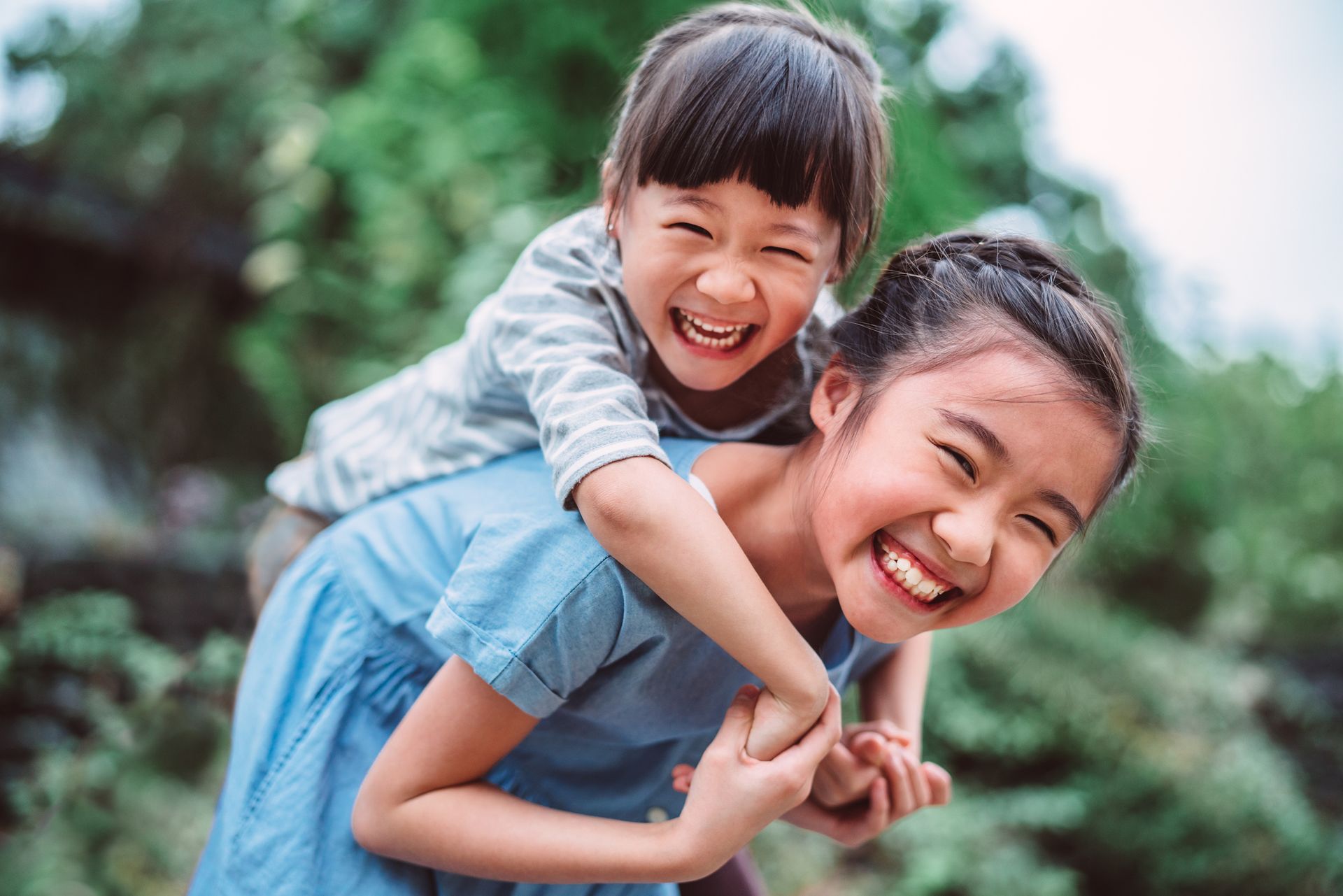 Two little girls are playing together and one of them is giving the other a piggyback ride.