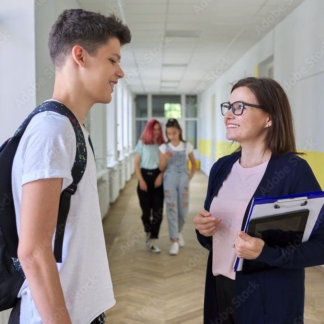 A teacher speaking with a student in a school hallway