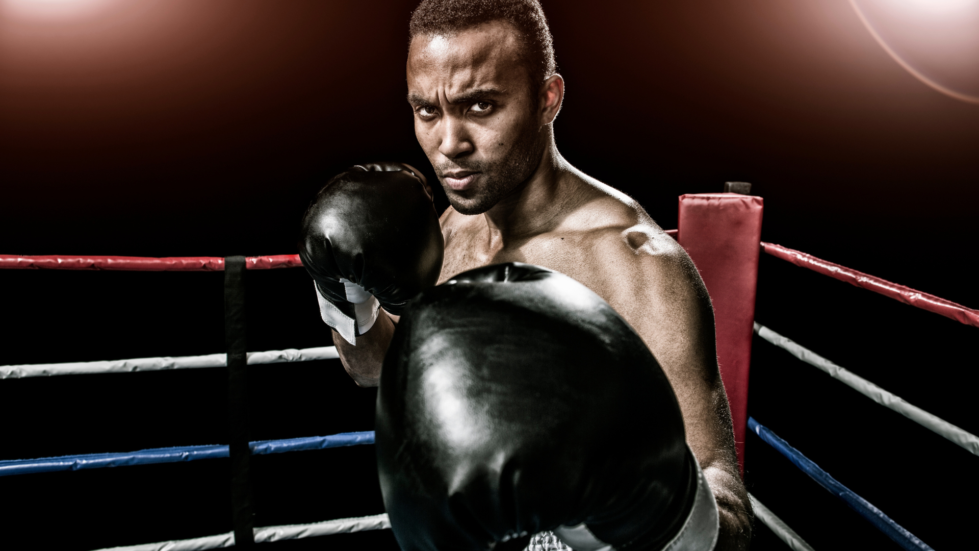 A man wearing boxing gloves is standing in a boxing ring.