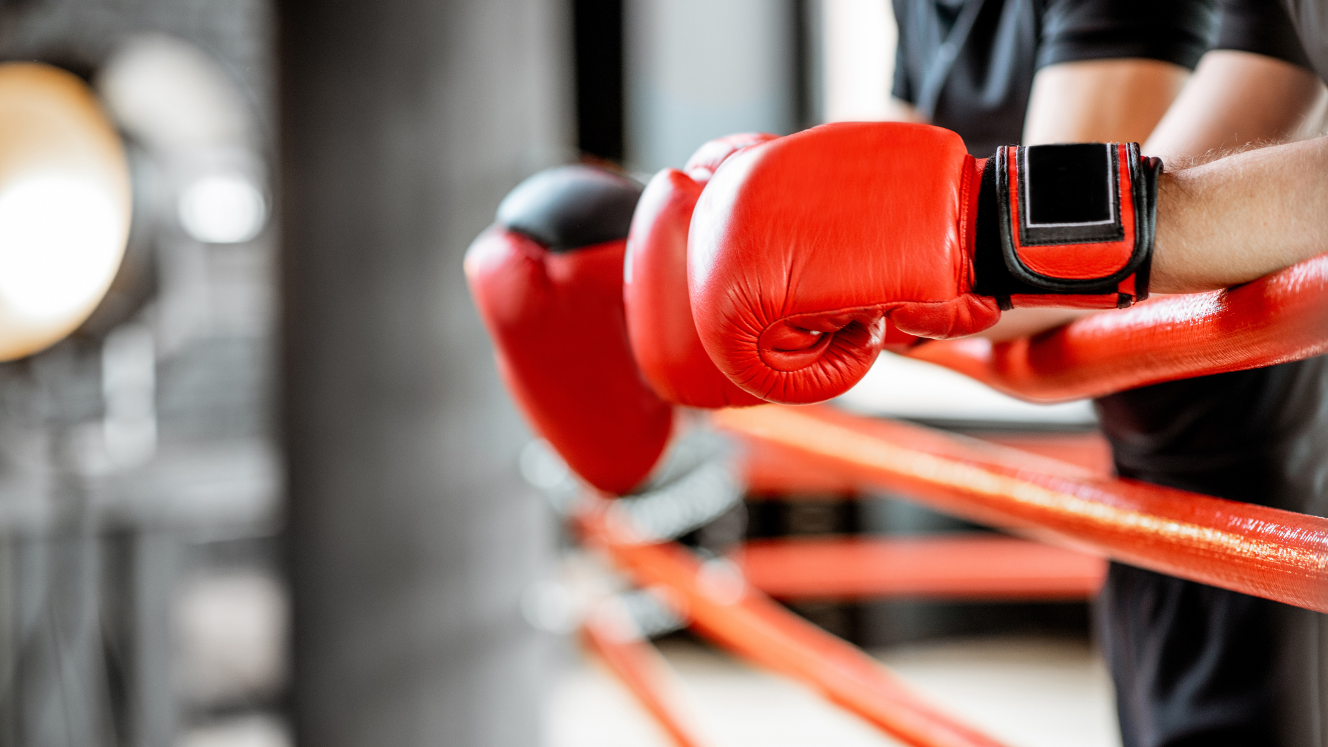 A man wearing boxing gloves and a smart watch is standing in a boxing ring.