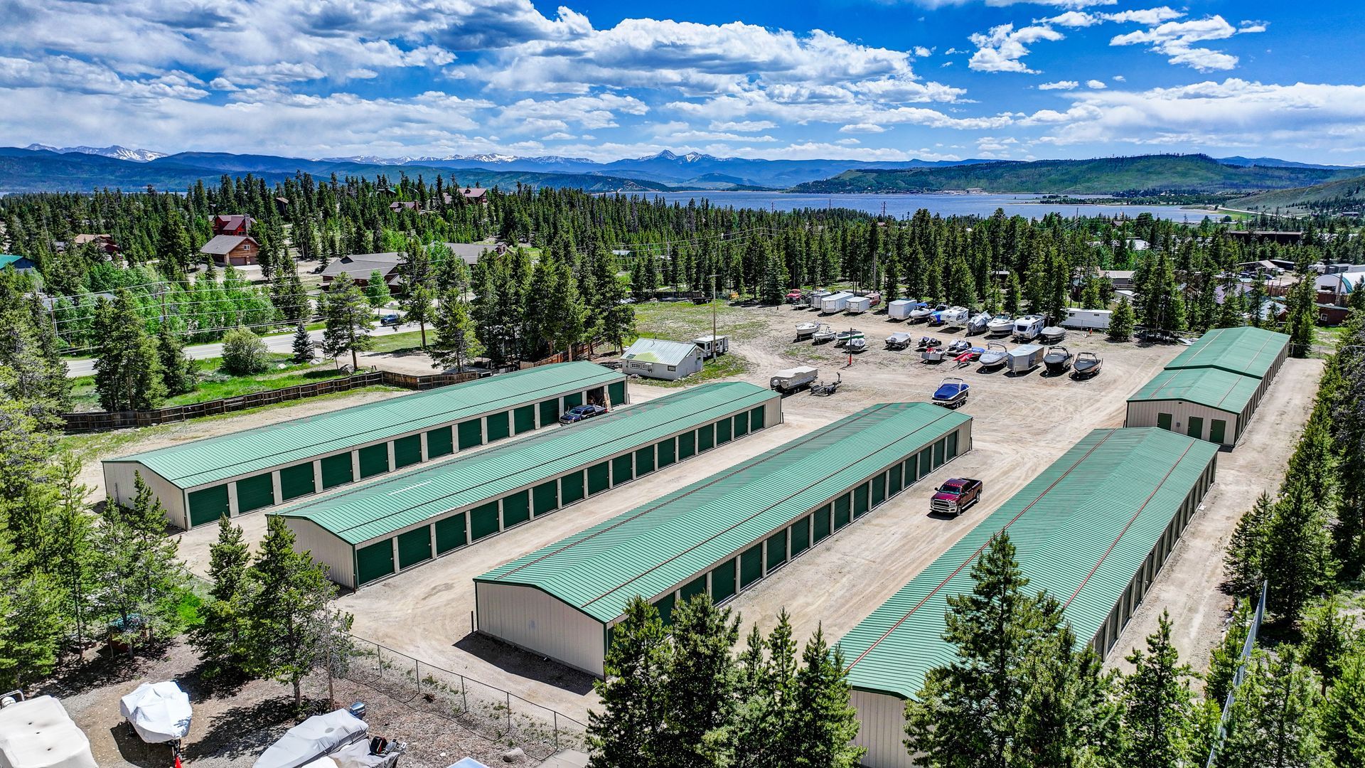 Storage units nestled among trees in a green, mountainous setting with water in the background.