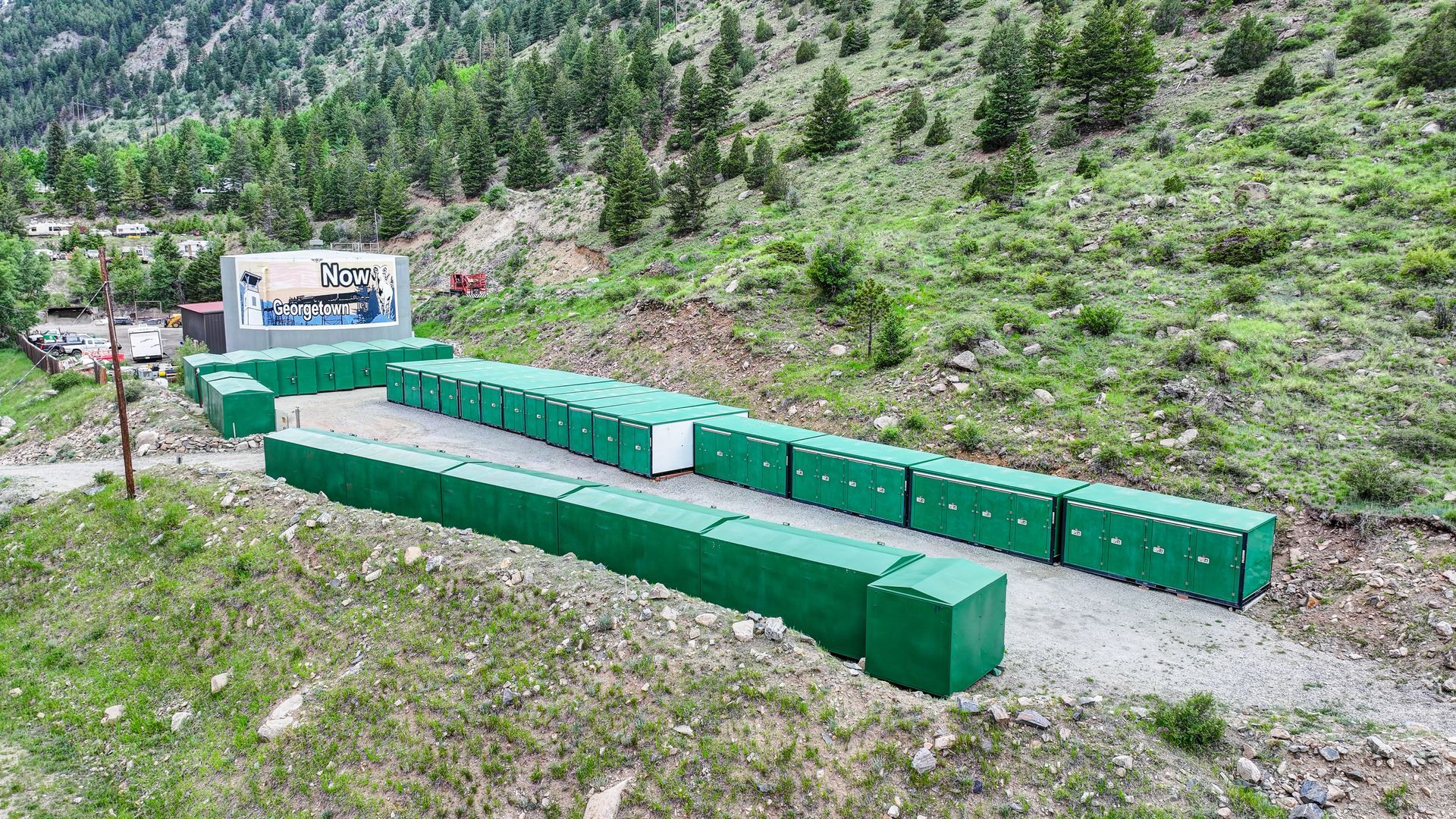 Storage units nestled among trees in a green, mountainous setting.
