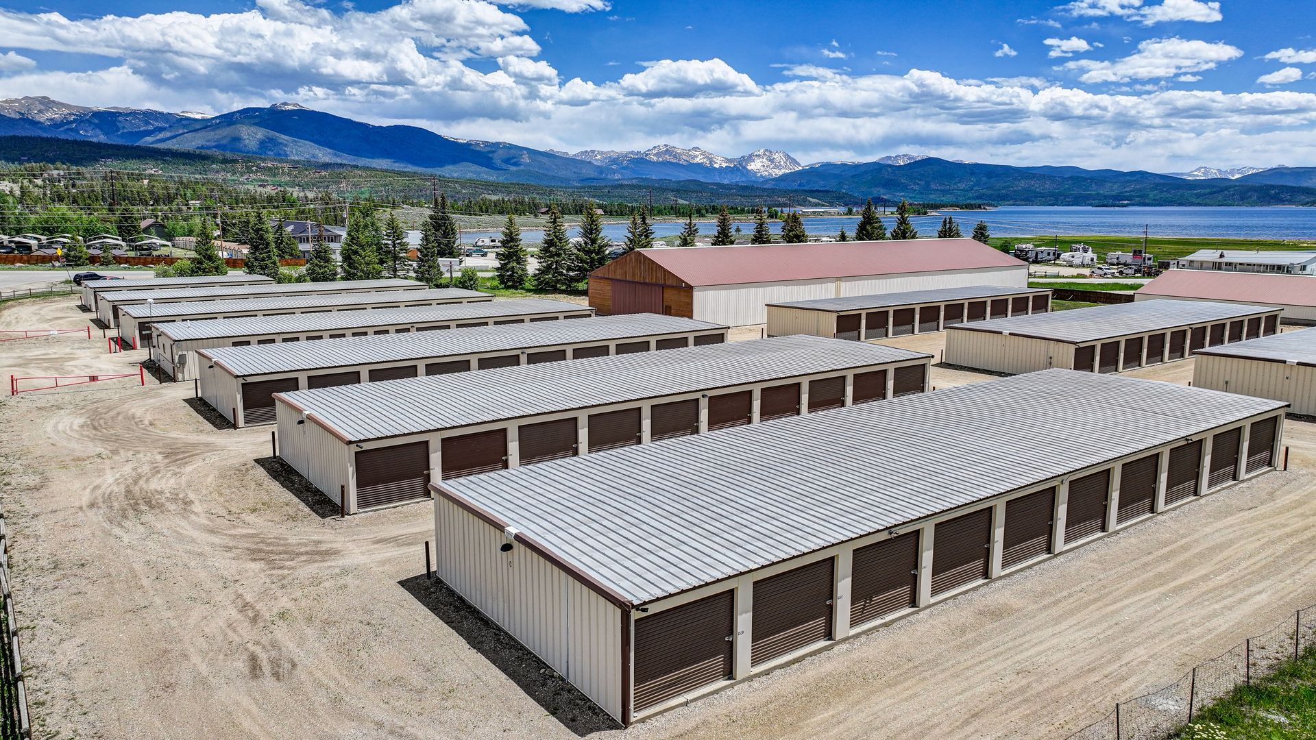 Storage units nestled among trees in a green, mountainous setting with water in the background.