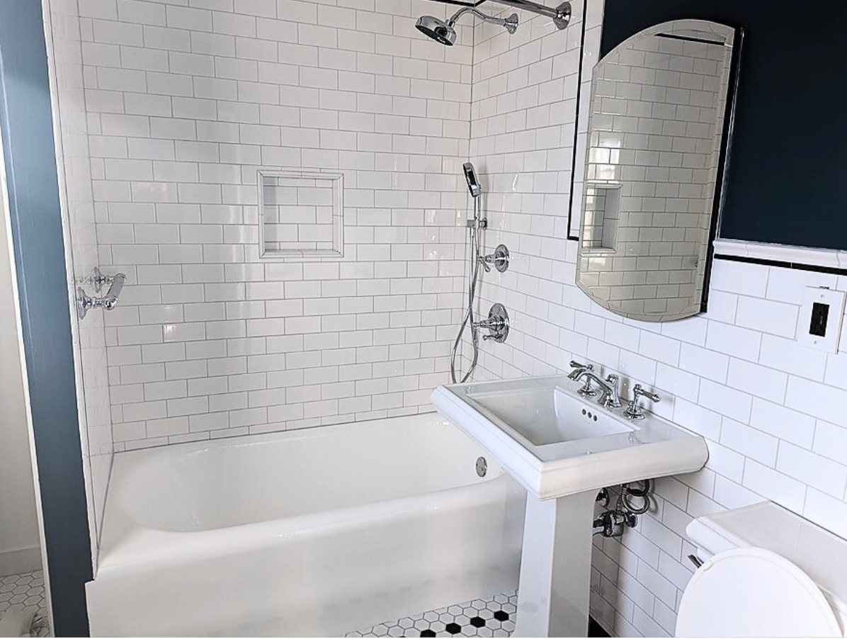 A bathroom with a tub, sink, toilet, and mirror