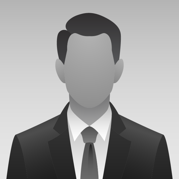 Smiling man in a gray suit and burgundy tie standing in a bright office, with a blurred background painting