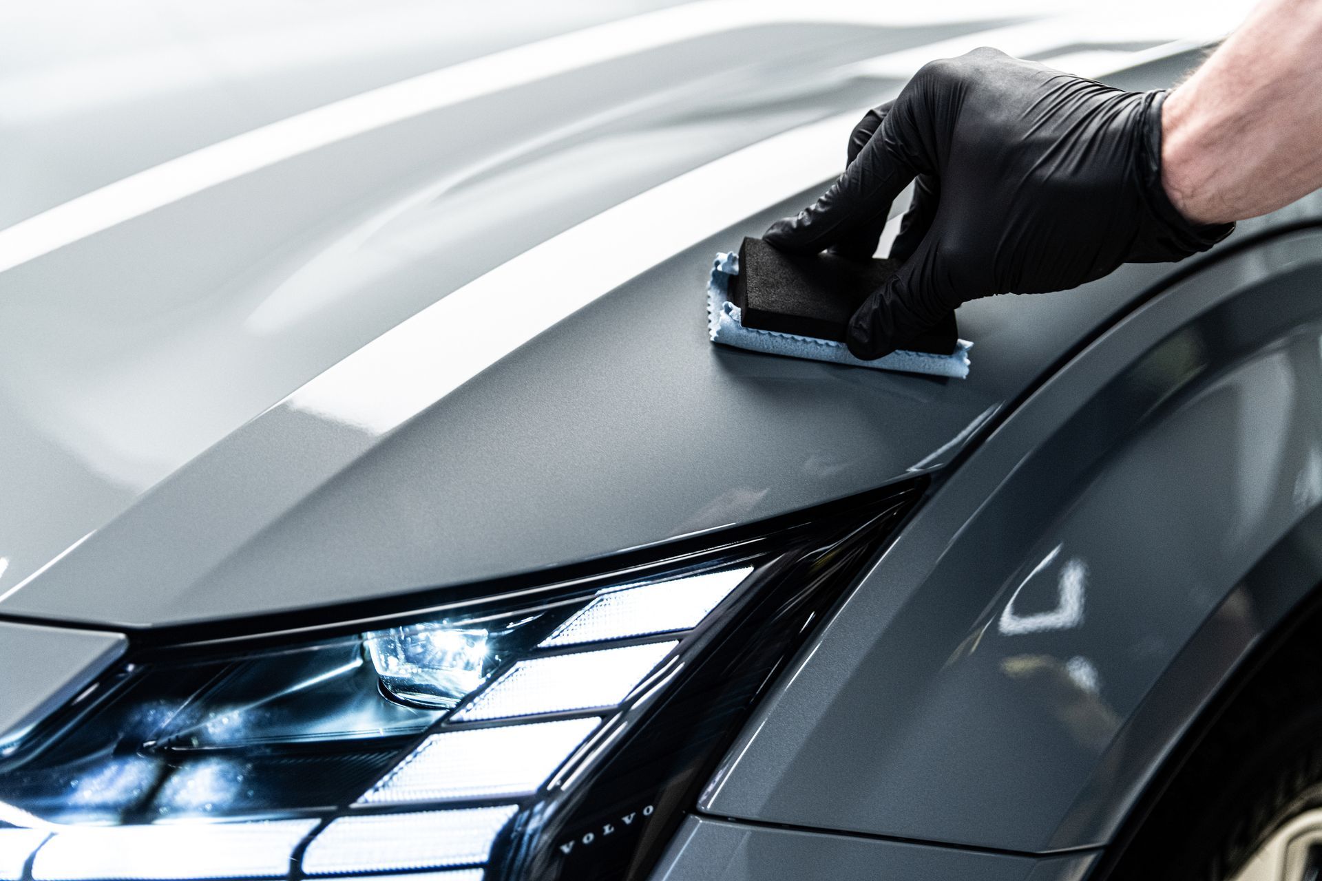 A person wearing black gloves is polishing the hood of a car.