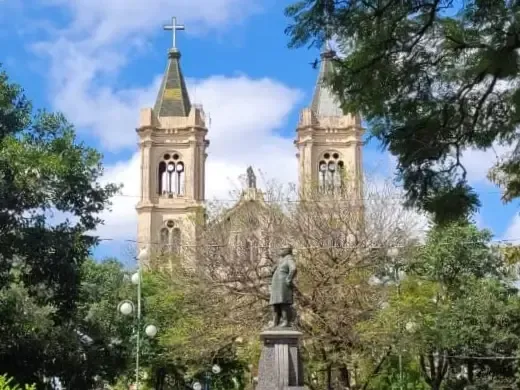 Igreja com torres gêmeas e uma estátua em um parque, céu azul com nuvens.