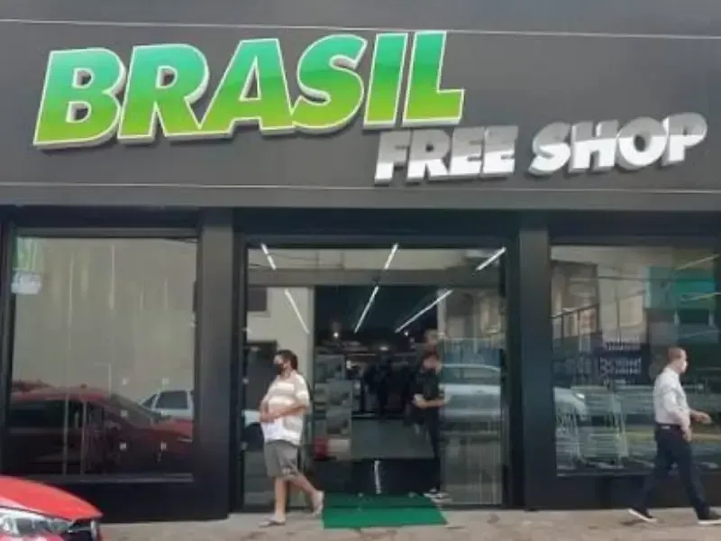 Fachada da loja Brasil Free Shop com pessoas passando. Placa verde e branca, prédio preto.