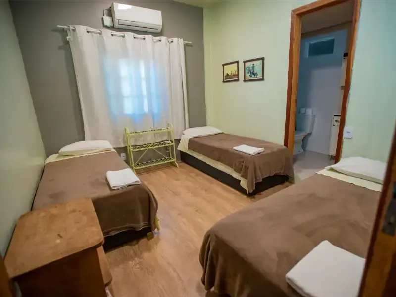 Um quarto com três camas, janela e porta para o banheiro.