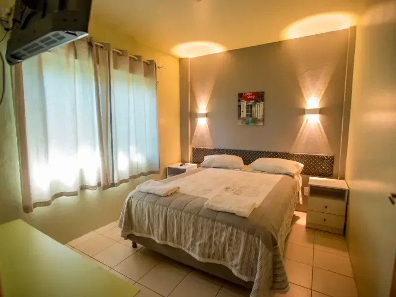 Quarto de hotel com cama, mesas de cabeceira e apliques de parede.