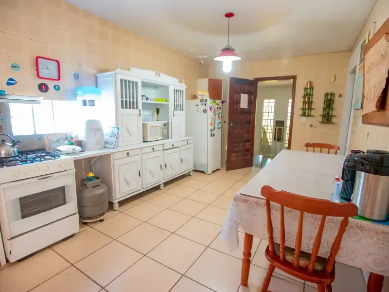 Cozinha com armários brancos, fogão, geladeira e mesa com cadeiras.