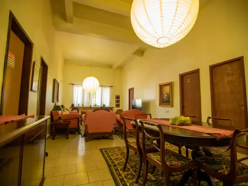 Interior espaçoso do hotel com mesa de jantar, cadeiras e área de estar sob grandes luminárias pendentes.