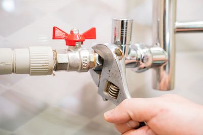 A hand using an adjustable wrench to tighten a metal valve connected to white plumbing pipes.