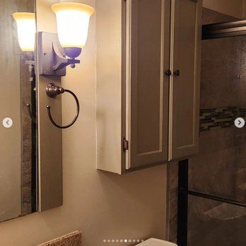 A bathroom with a toilet , sink , mirror and cabinets.