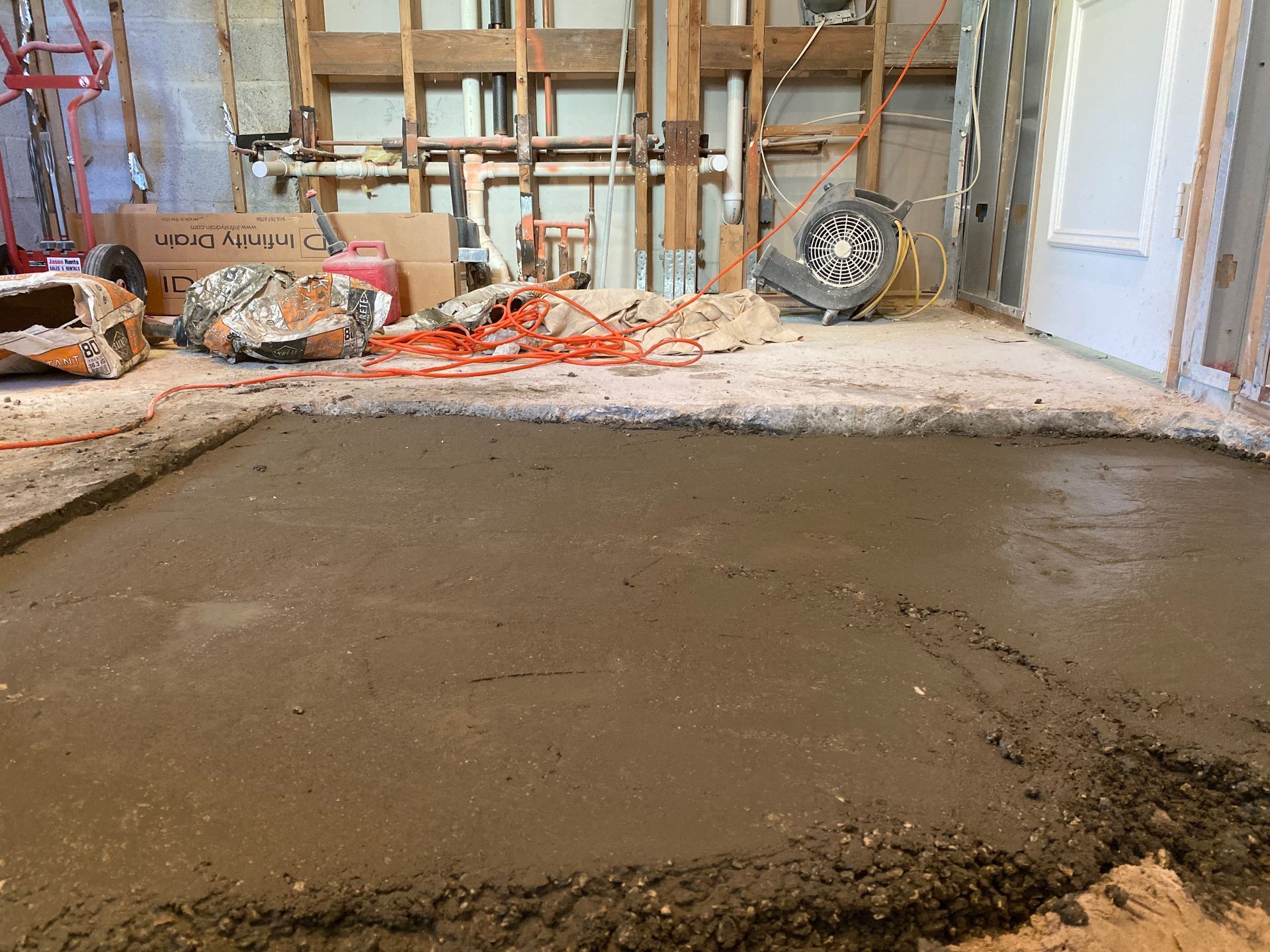 Freshly poured concrete floor in a room under construction, with exposed studs and equipment.