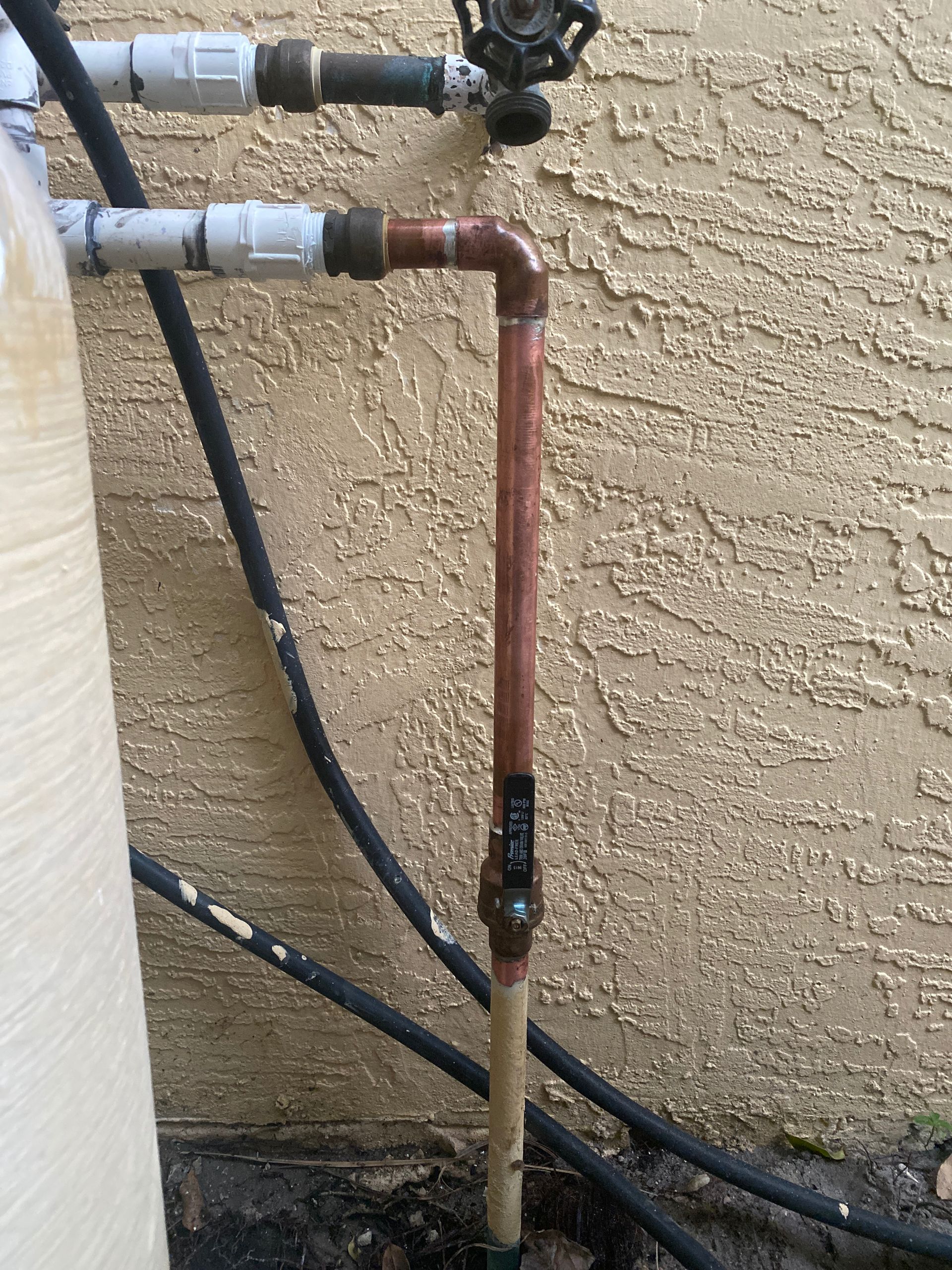 Copper pipe section connected to water pipes against a stucco wall.
