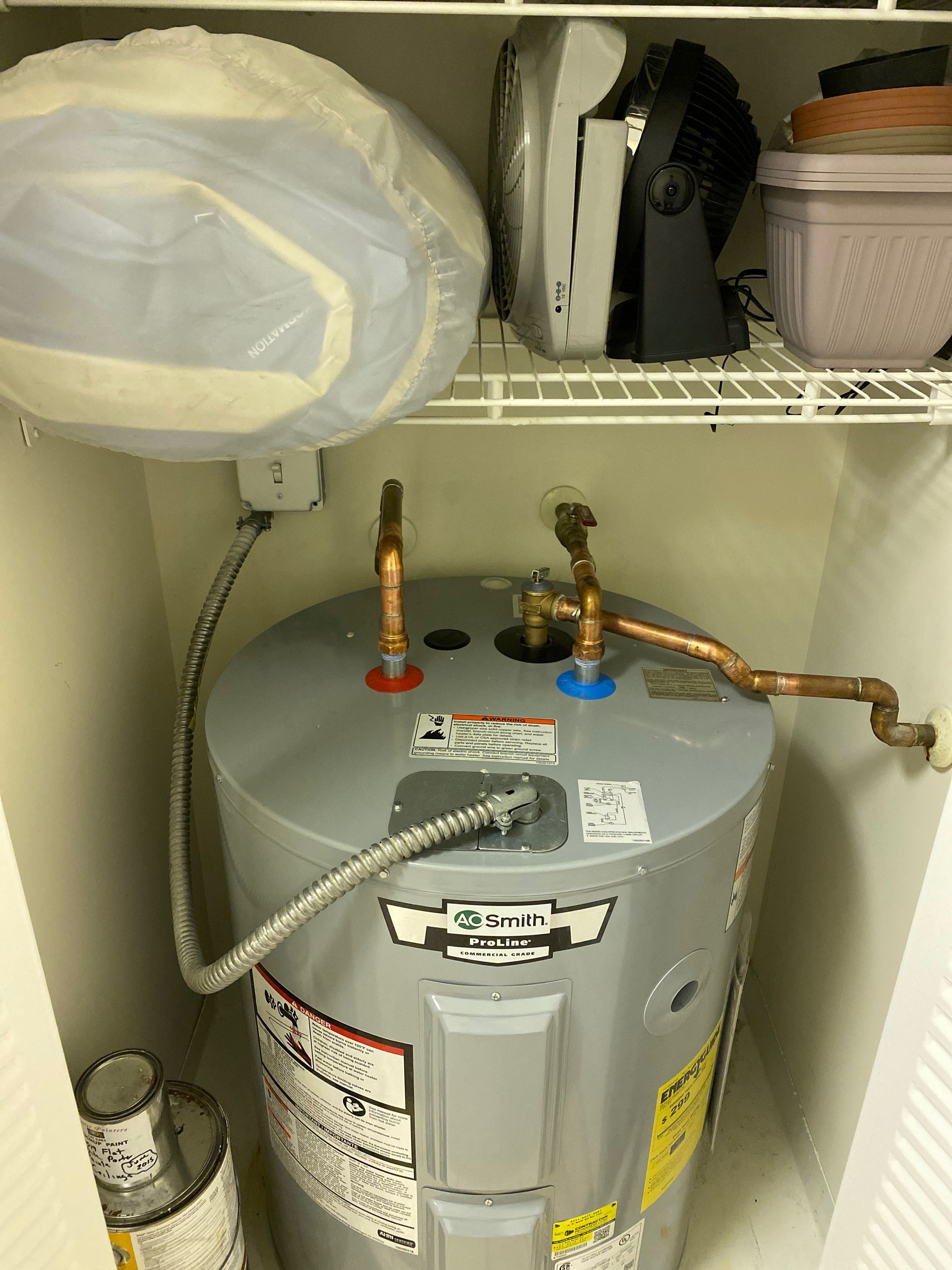 Water heater in a closet. Includes copper pipes, electrical wiring, and items stored on a shelf above.