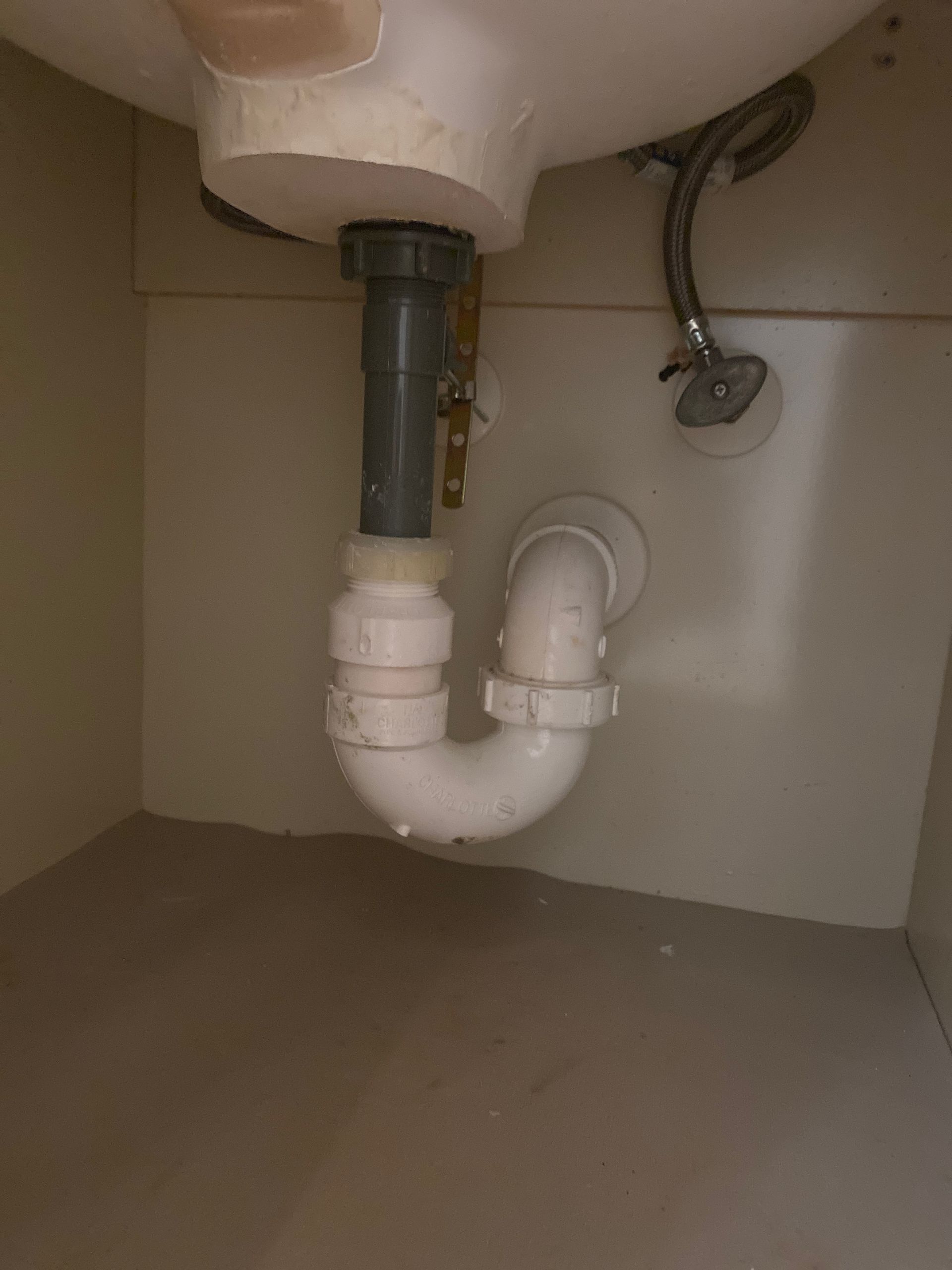 Underside of a bathroom sink showing white plumbing pipes. The pipes include a p-trap and drain.