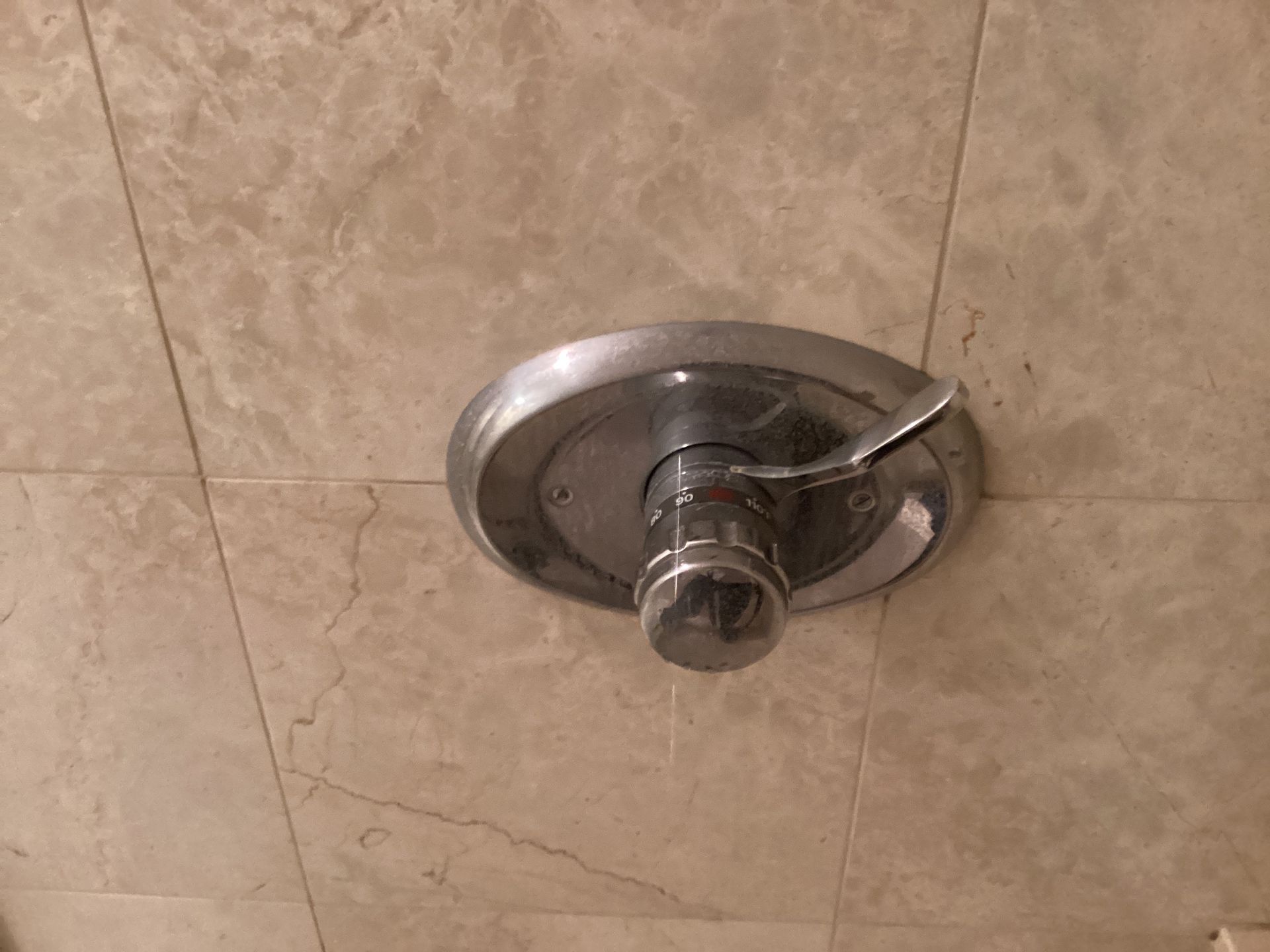 Chrome shower valve with lever handle on a beige tiled wall.