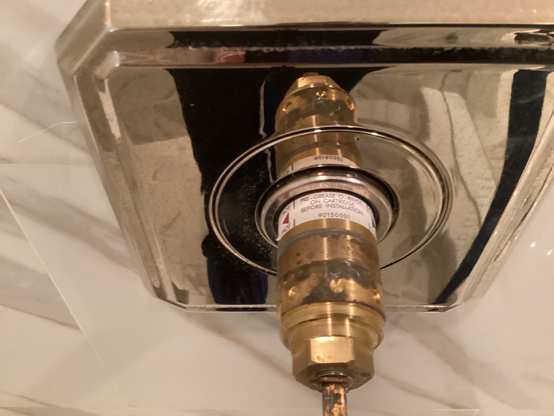Close-up of a brass shower valve and a silver decorative plate against a white tiled wall.