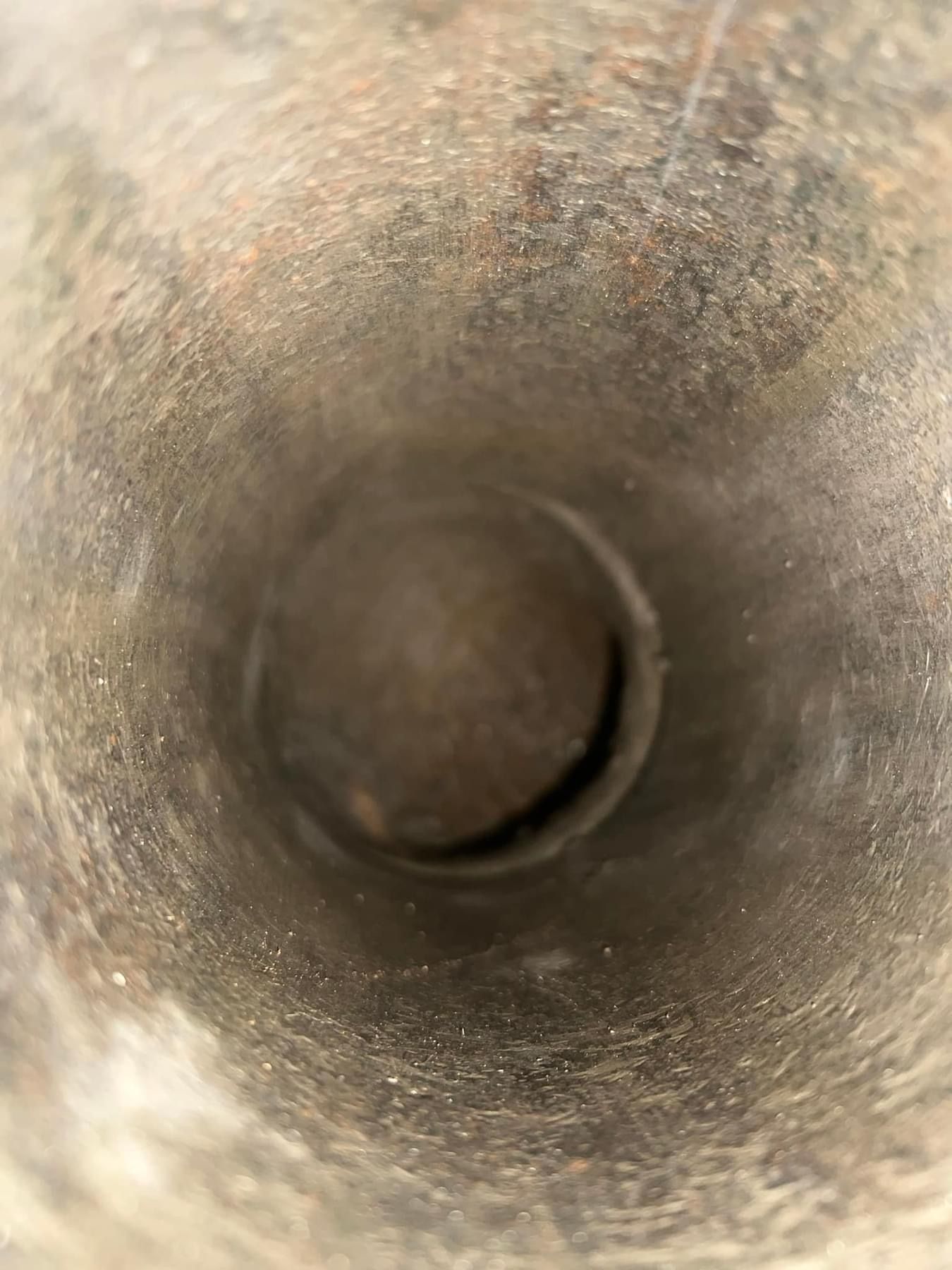 Inside of a rusty metal cylinder, looking towards a dark circular opening.