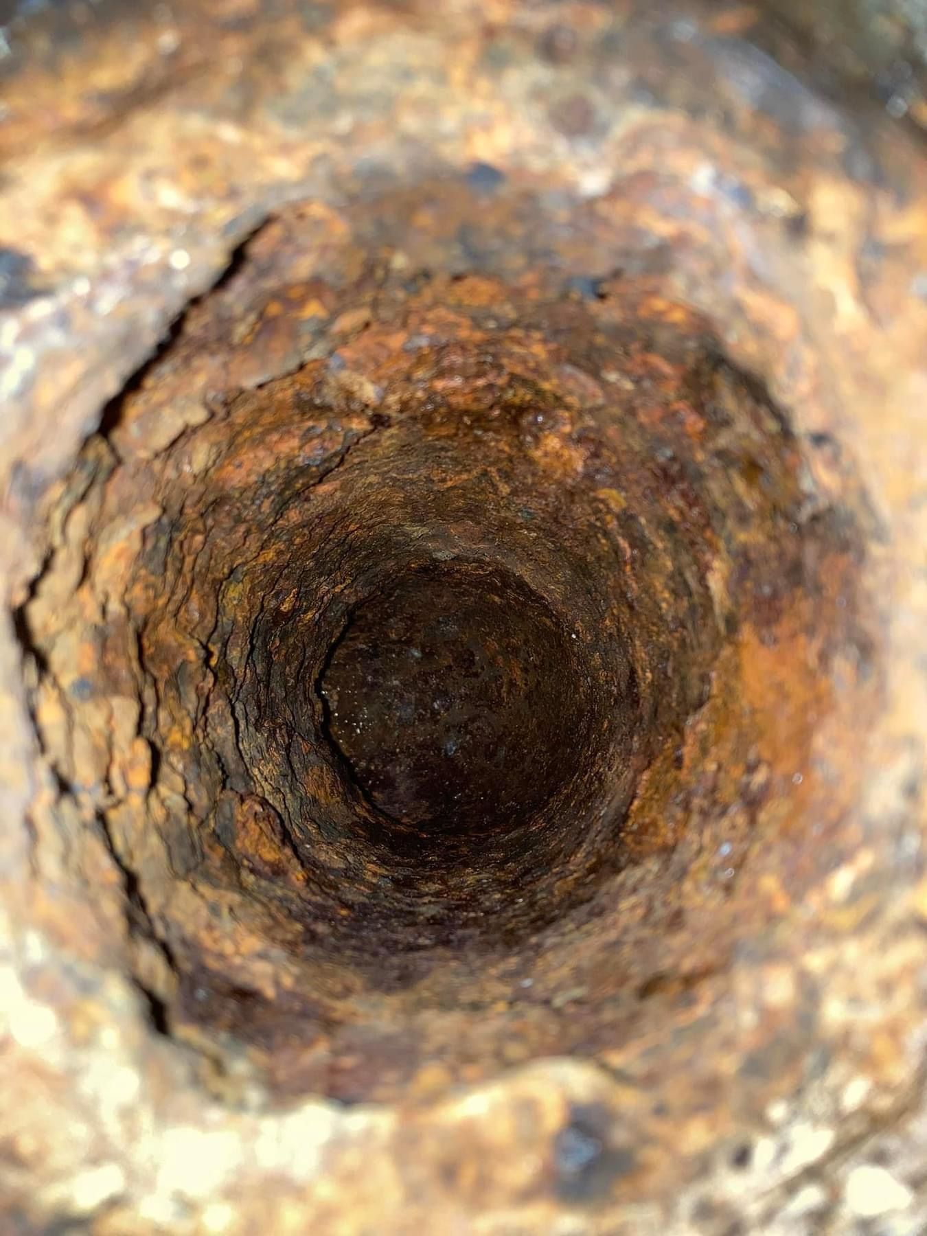 Rusting metal pipe, looking down into a dark, cylindrical cavity.