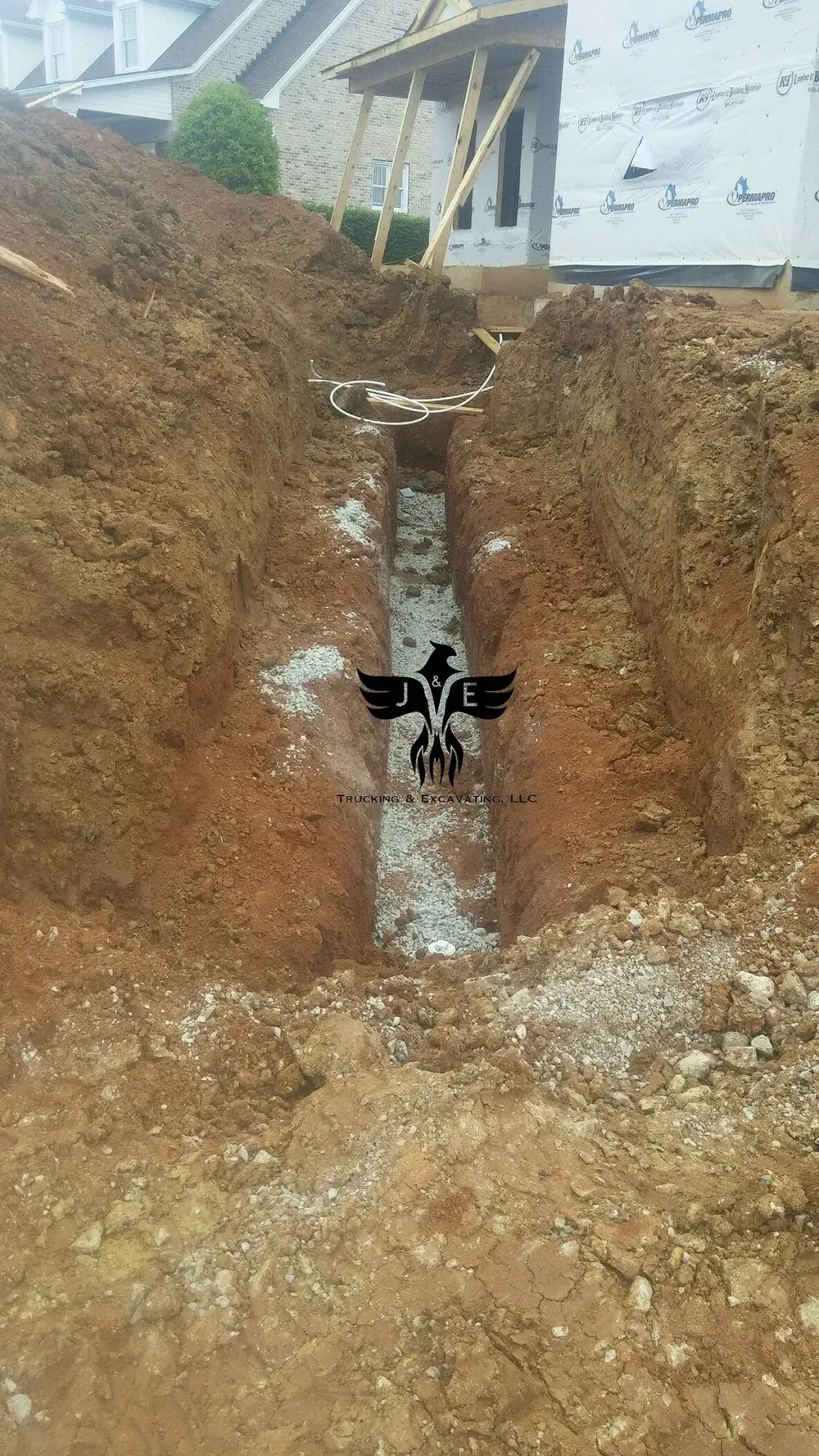 Deep excavation trench with exposed soil and a white drainpipe beneath a building foundation