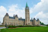 Parliament Buildings in Ottawa, Canada. Stone structure with clock tower and green lawn. Blue sky background.