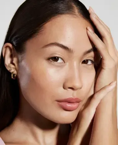 Woman with glowing skin, hand on face, light background.