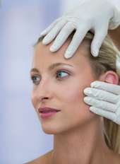 Woman's face examined by gloved hands, indoors.