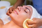 Woman receiving facial treatment; hands applying cleansing pads to face in spa.