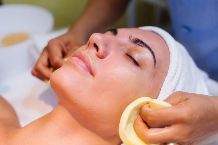 Woman receiving facial treatment; hands applying cleansing pads to face in spa.