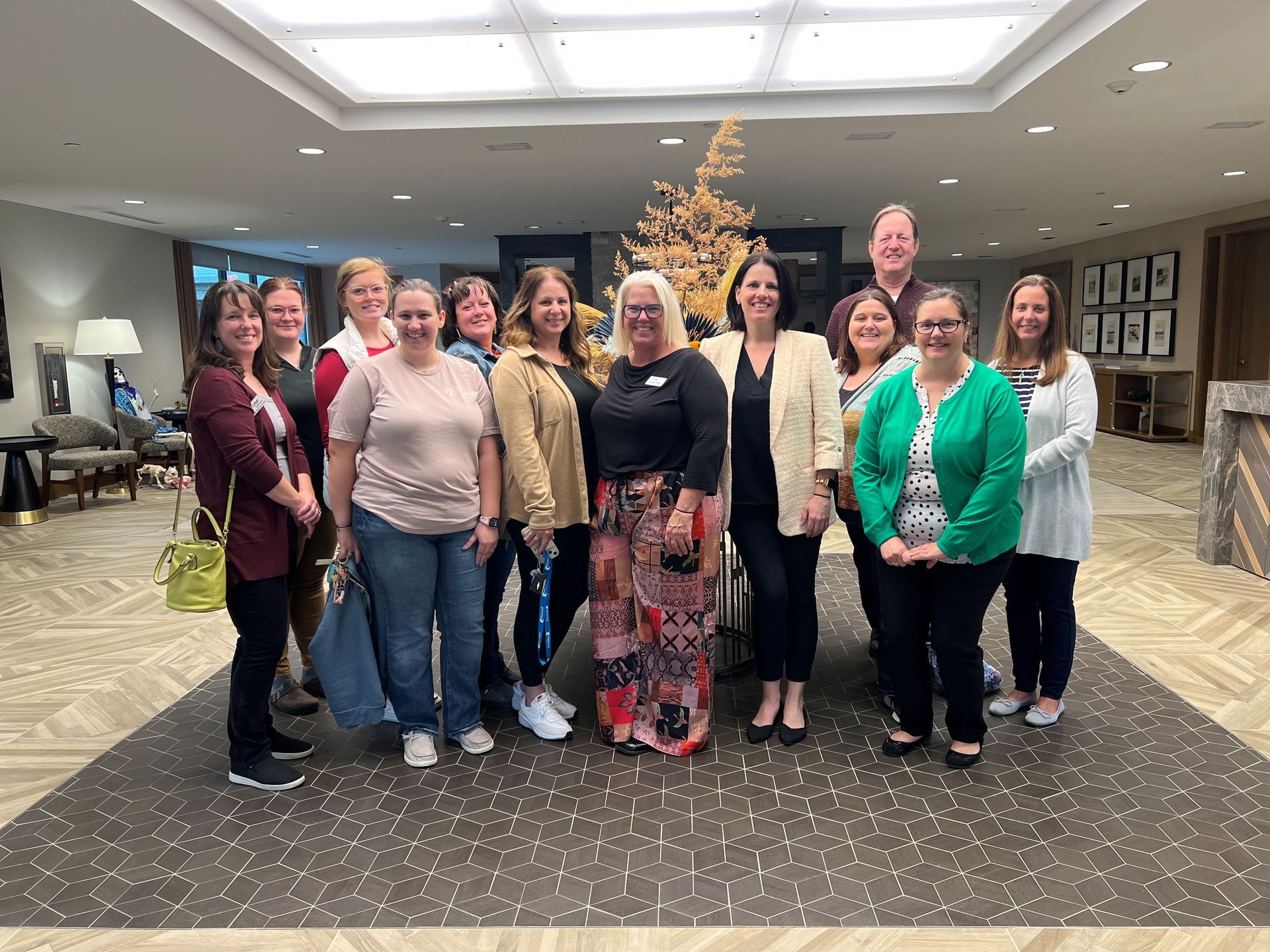 Group of people posing in a lobby. Some smile. Gold-colored festive decor in background.