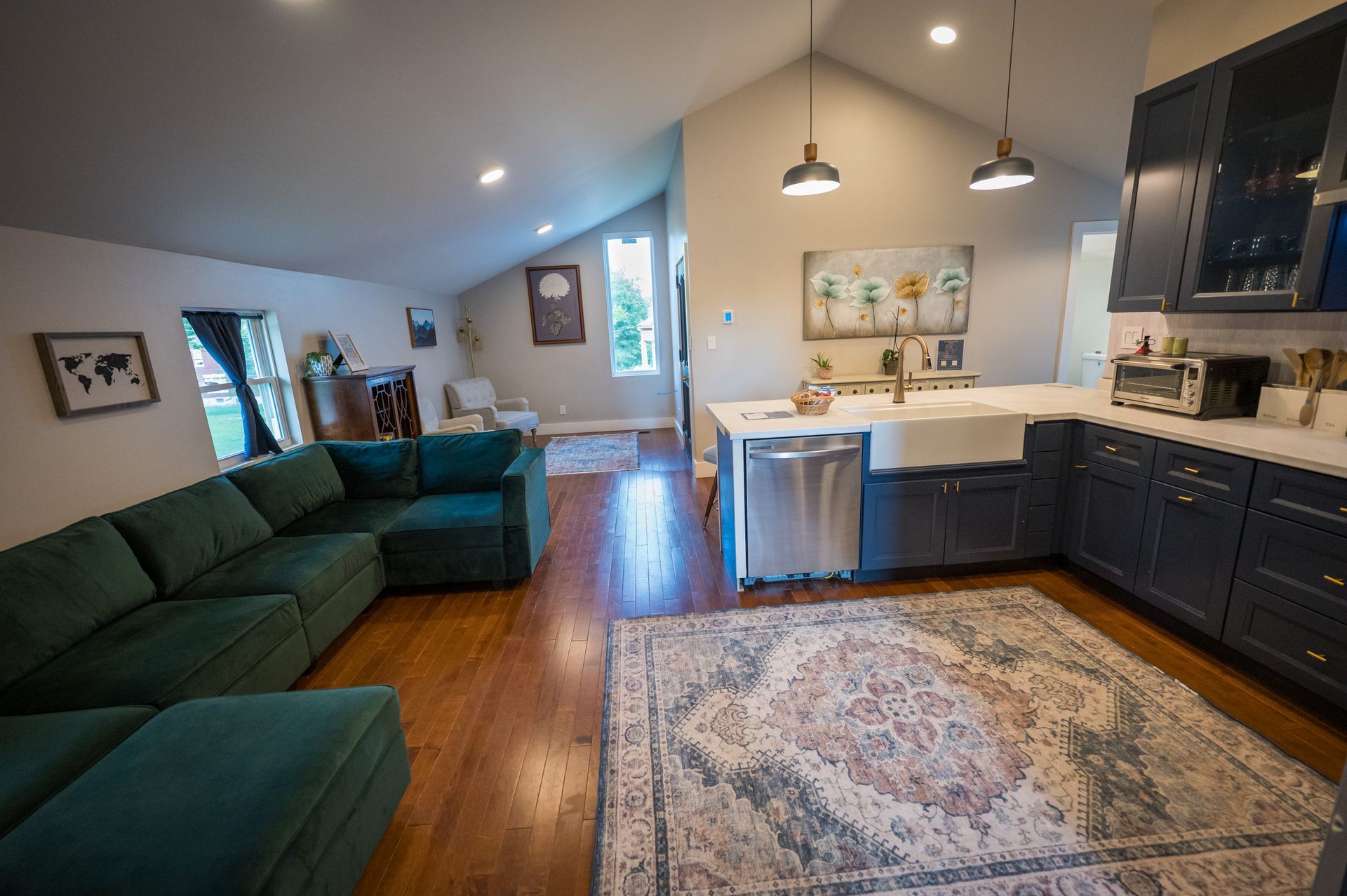 Open-concept living space with teal sectional, dark blue kitchen cabinets, and wood flooring.