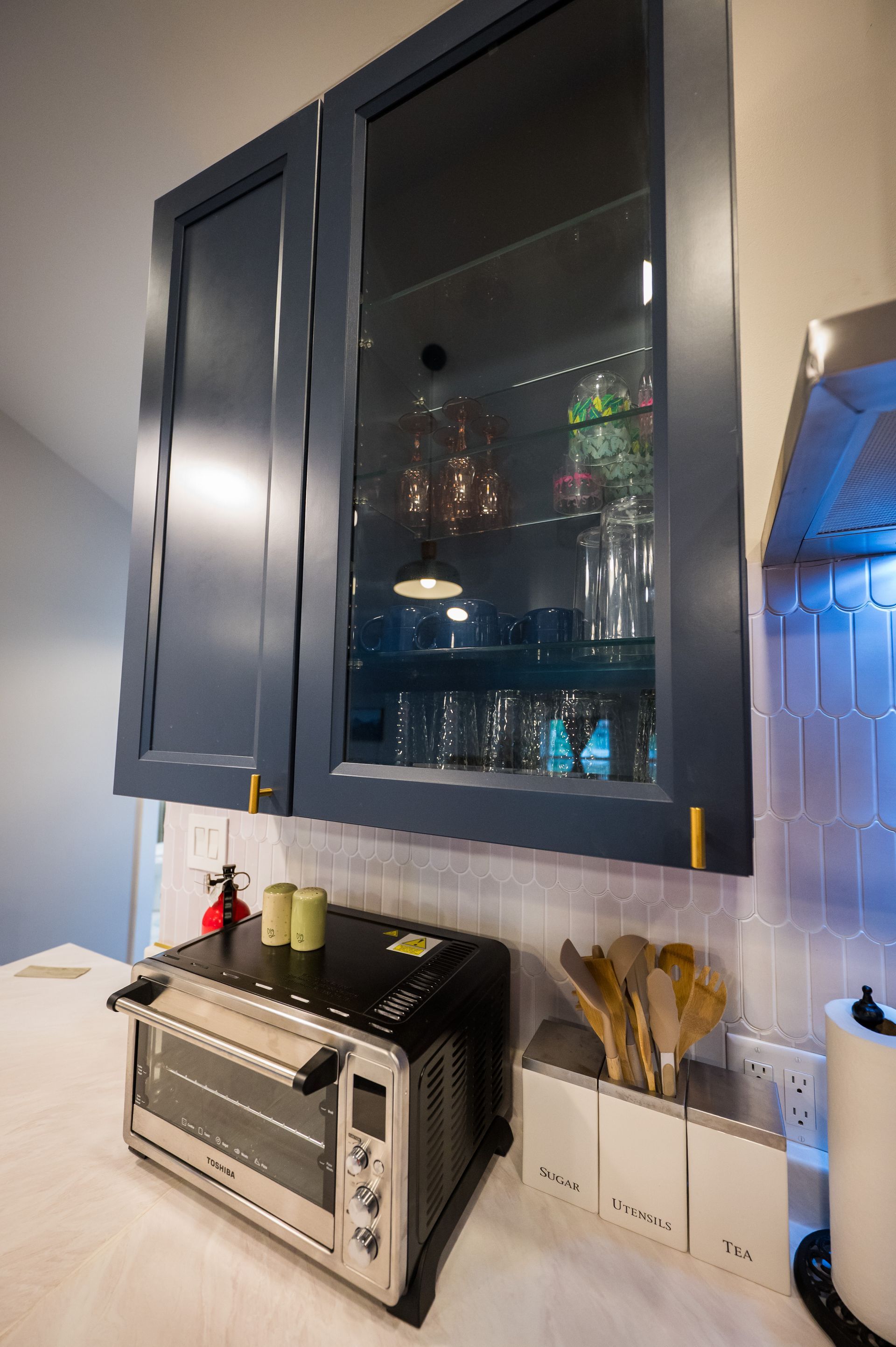 Blue kitchen cabinets with glass doors over a countertop with a toaster oven and utensils.