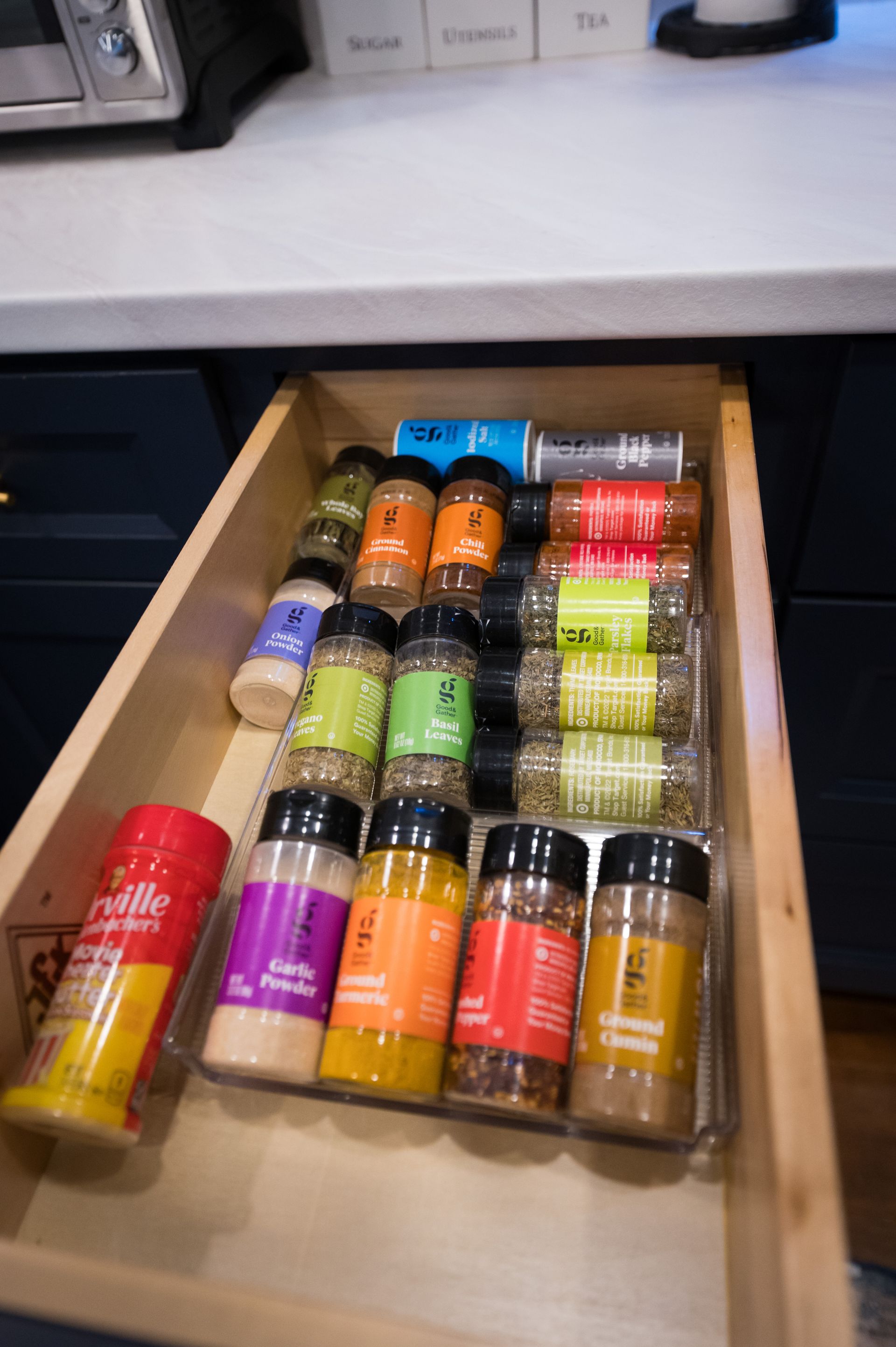 A kitchen drawer open, filled with various spice jars in clear organizers.