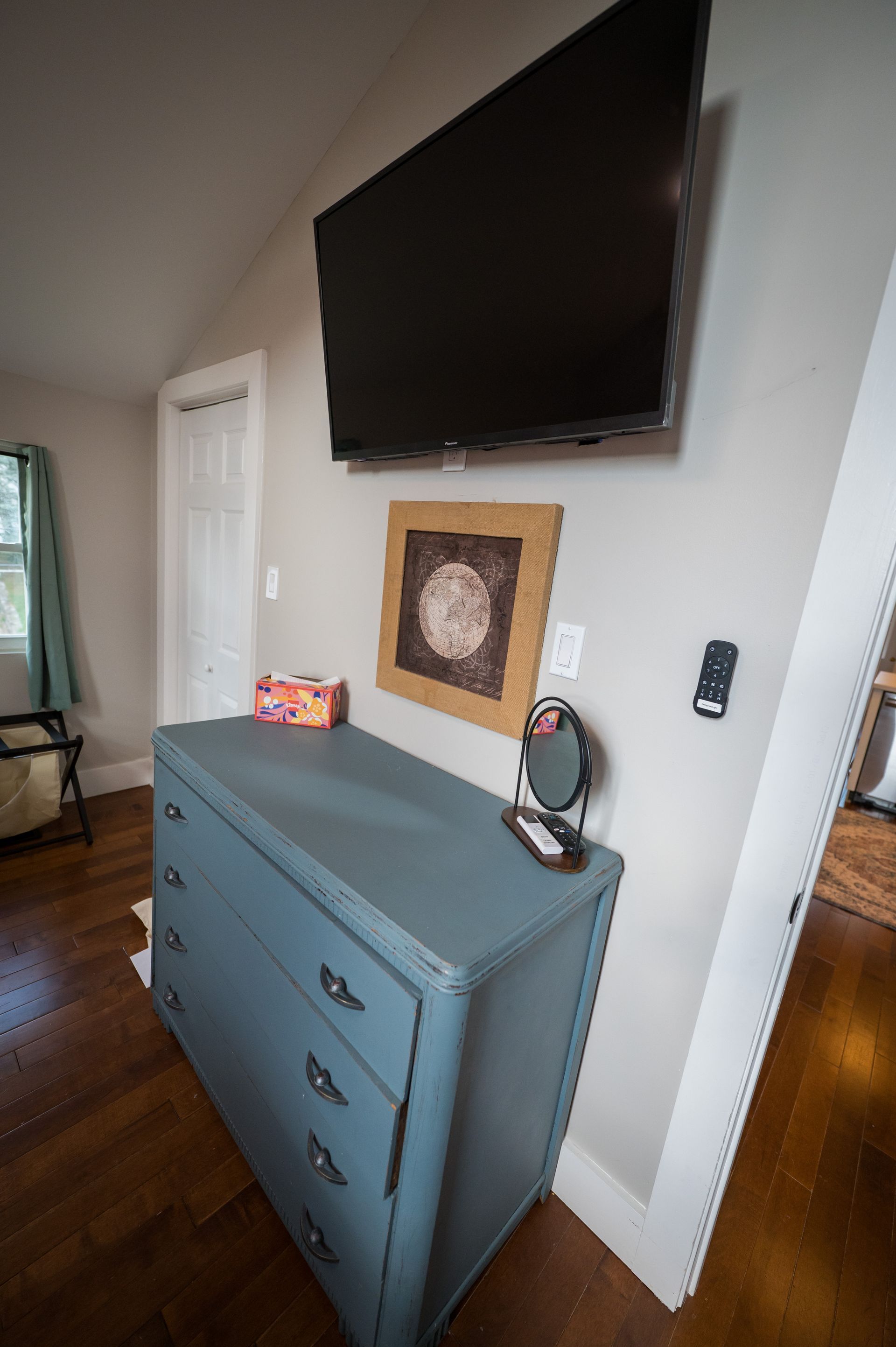 Blue dresser under a mounted TV and artwork in a bedroom.