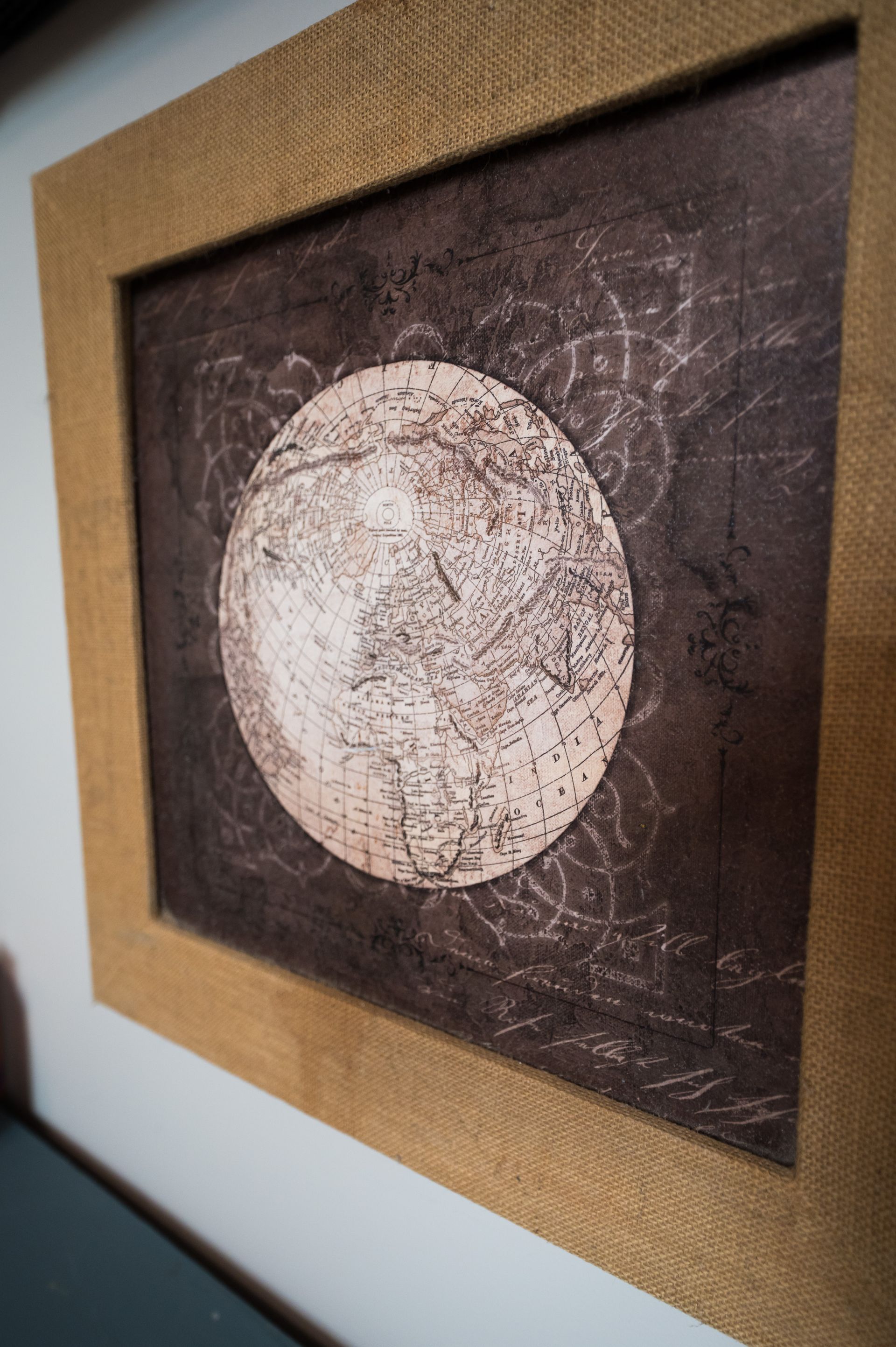 Framed artwork of a circular map in earth tones, with a decorative burlap frame.