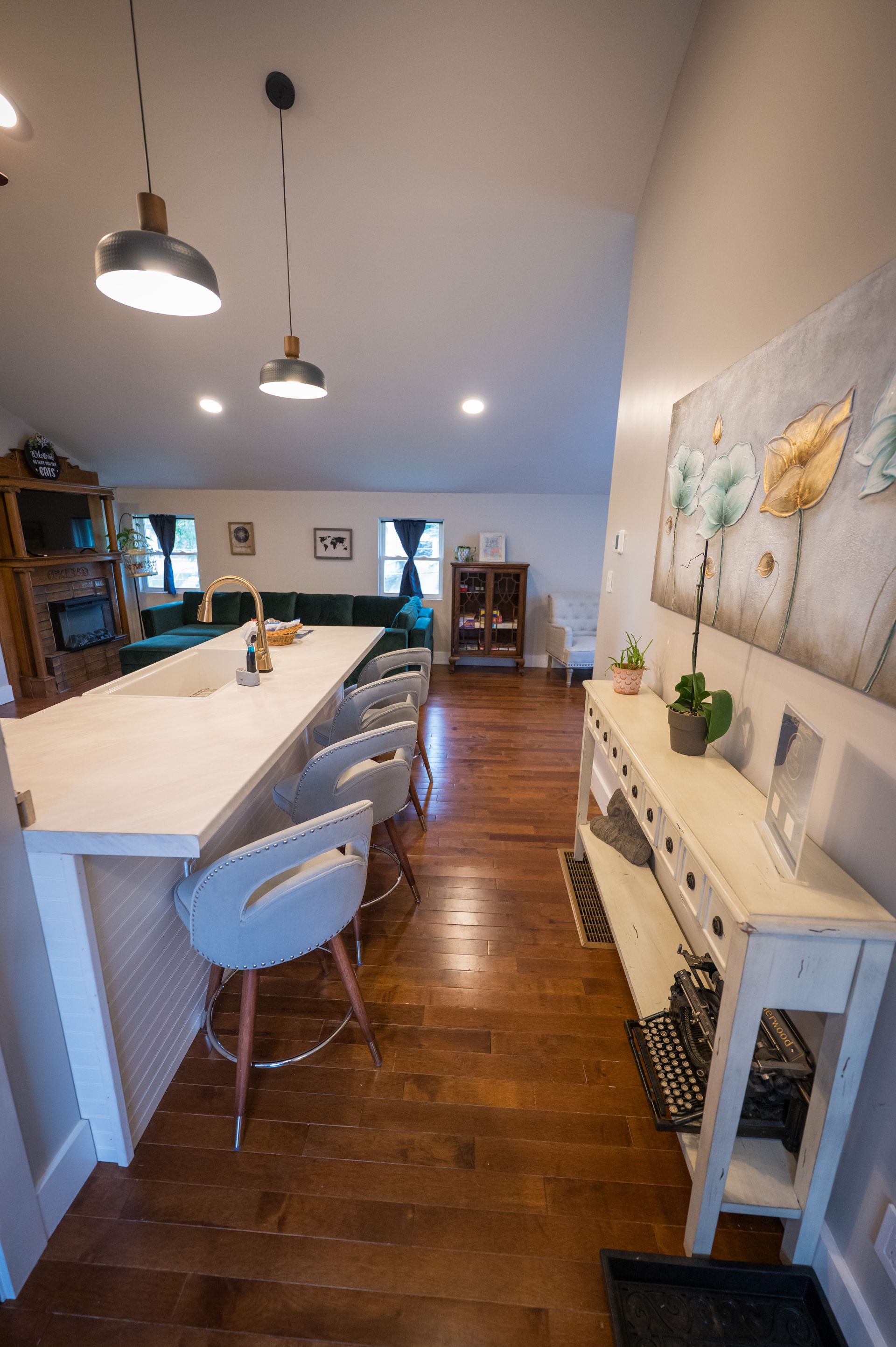 Open-concept kitchen with island and bar stools, leading to a living area with a sofa. Hardwood floors and white cabinets.
