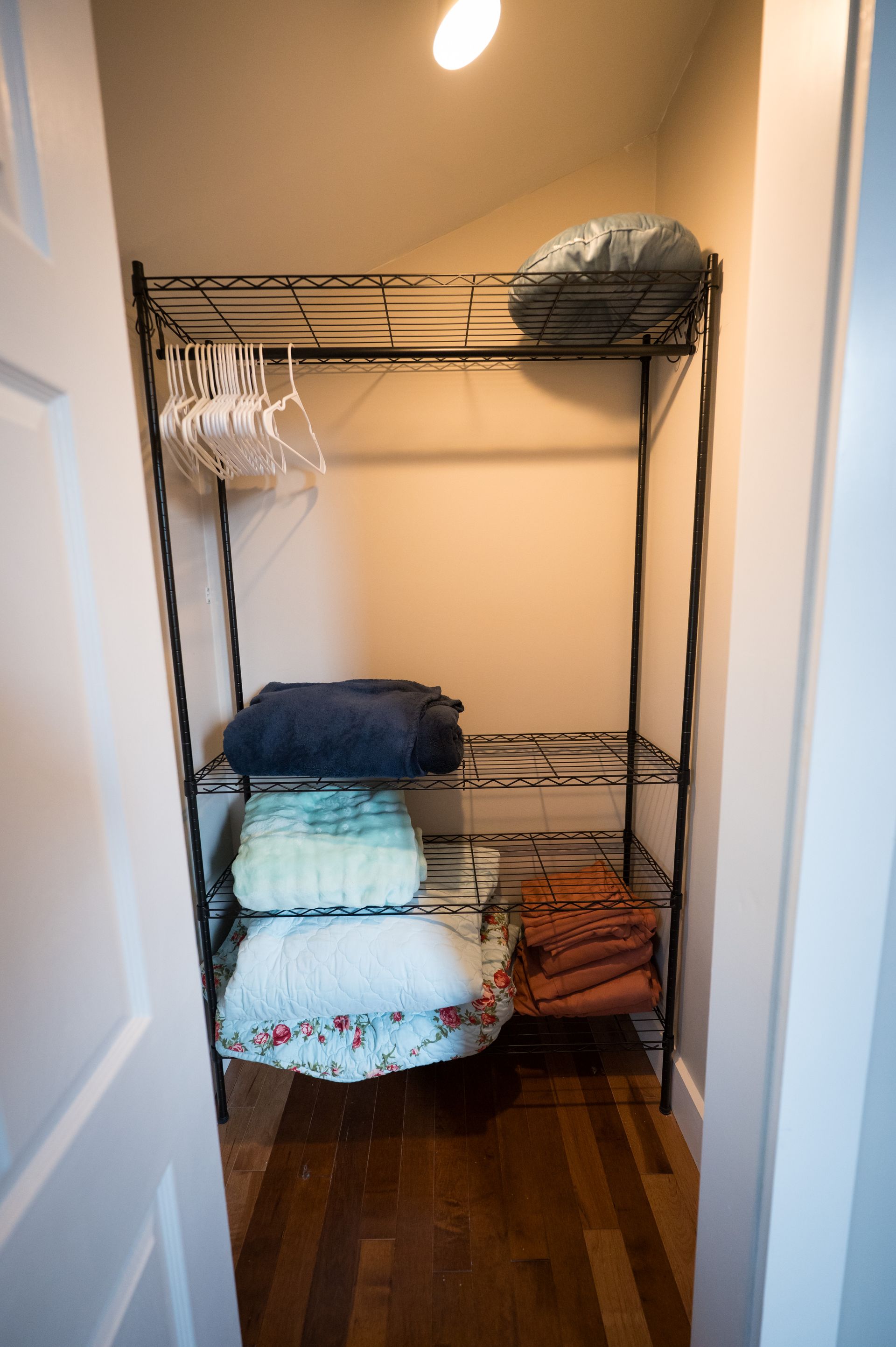 Narrow closet with wire shelves holding folded clothes and empty hangers.
