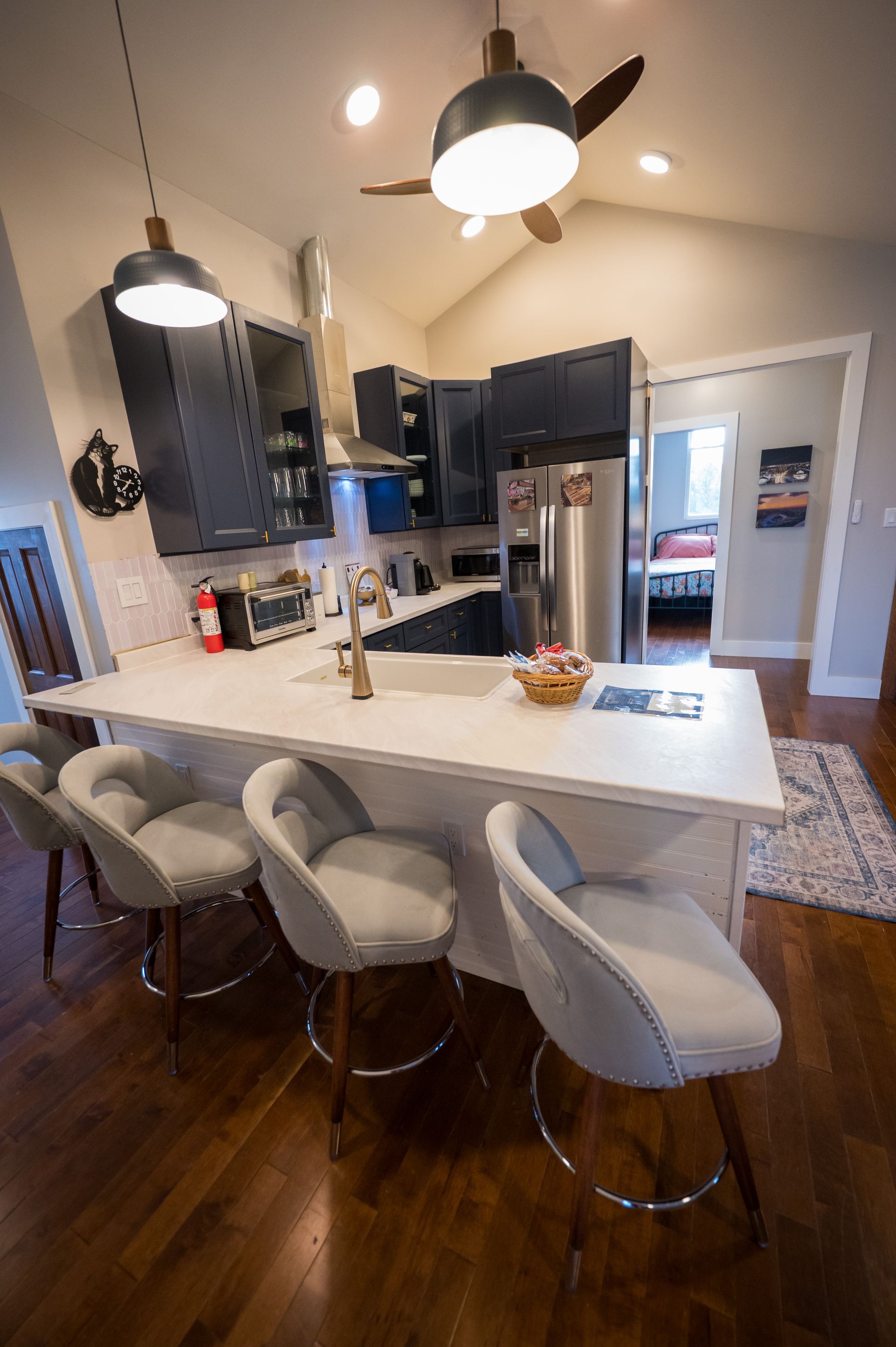 Kitchen with white countertop island, dark cabinets, stainless steel appliances, and gray bar stools.