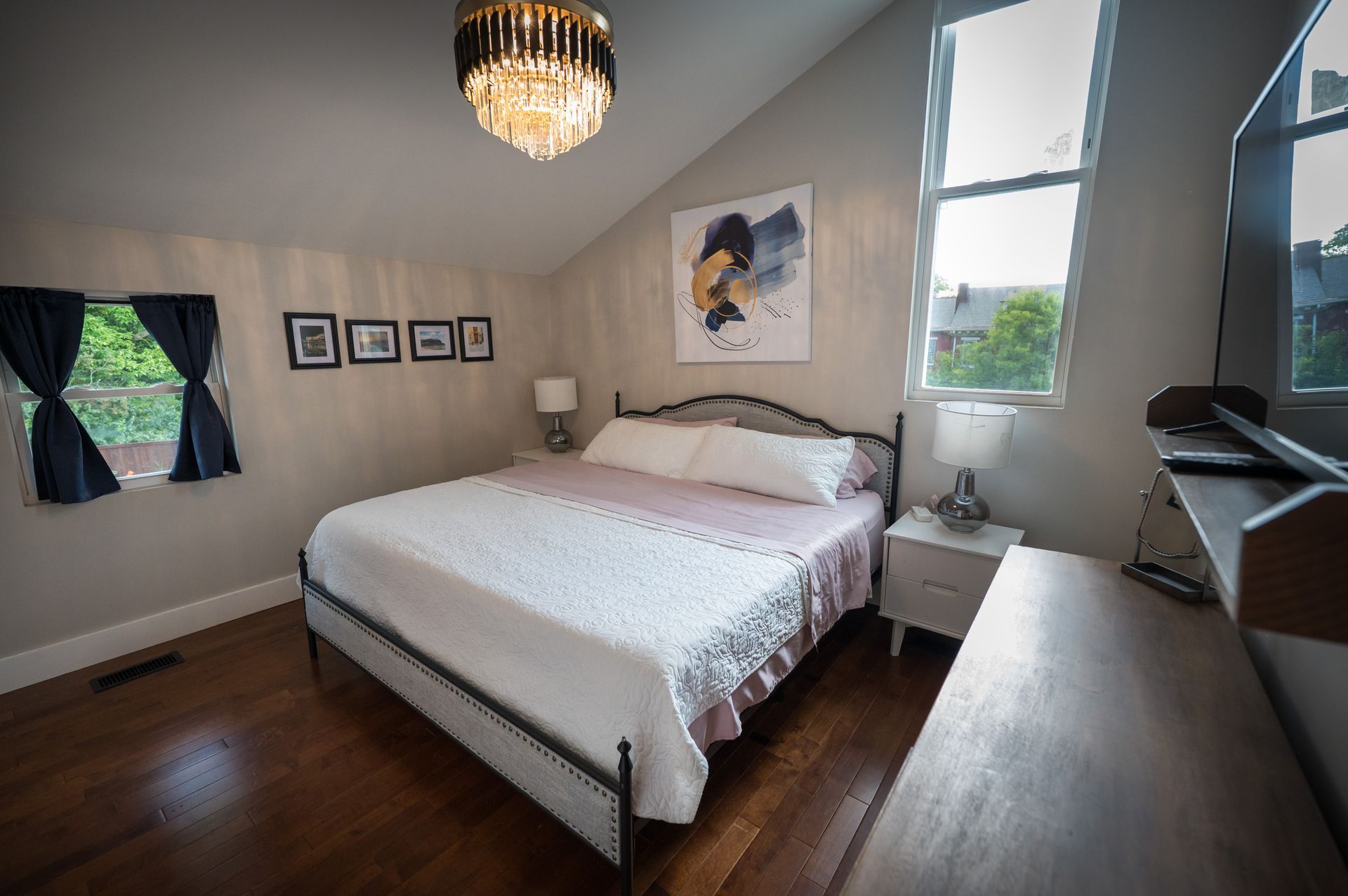 Bedroom with a bed, dresser, window, and artwork. Features a chandelier, hardwood floors, and gray walls.