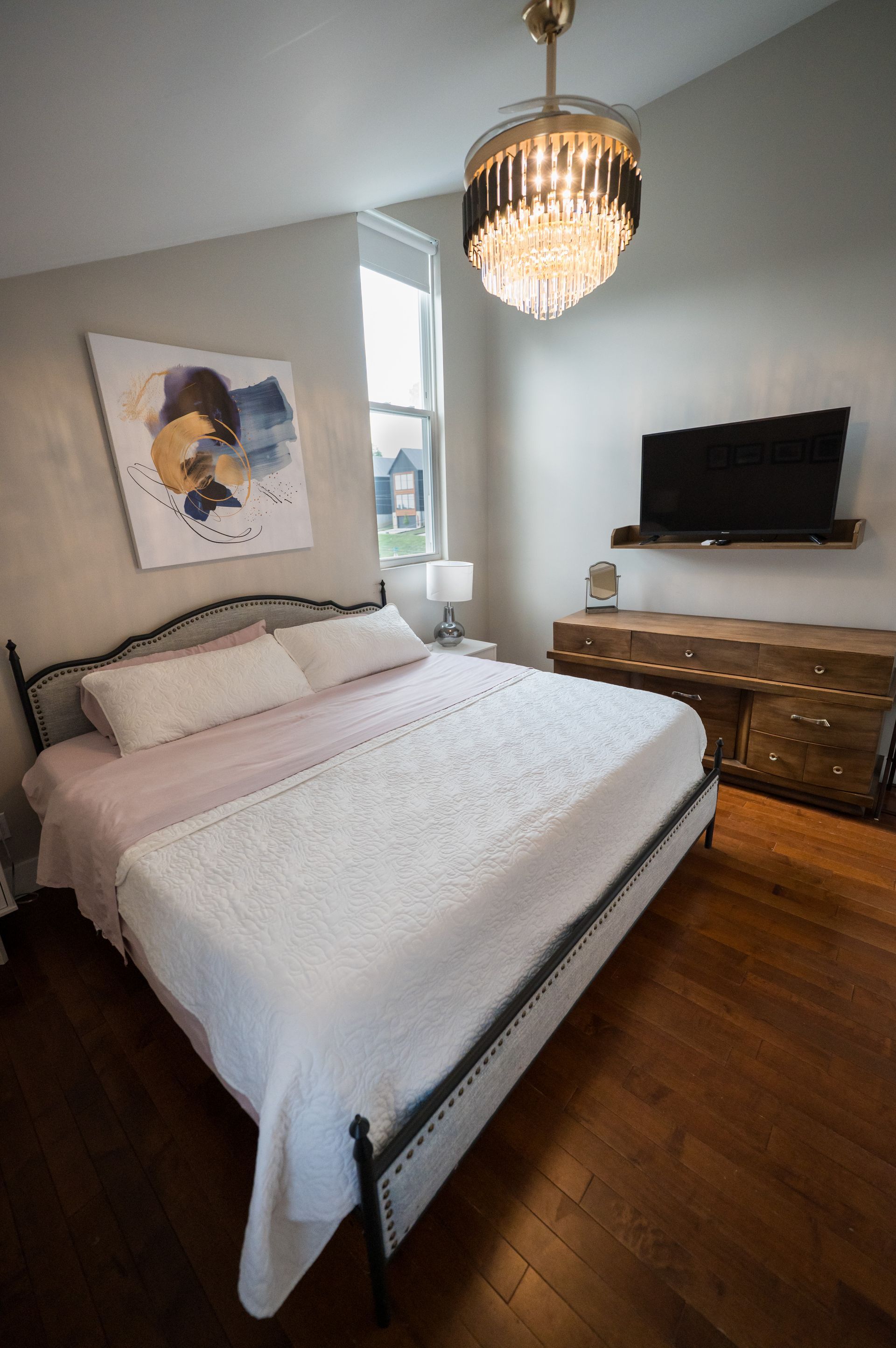 Bedroom with bed, art, TV, and crystal chandelier.